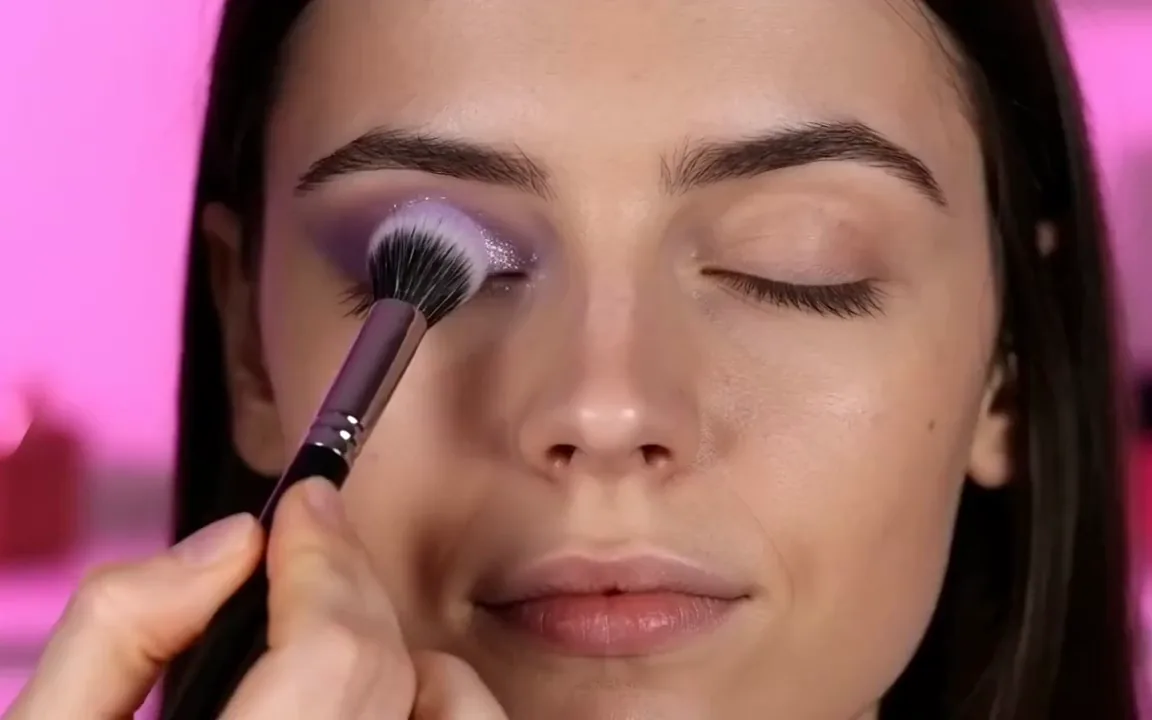 FLUX 3 video of a brush sweeping violet glitter eyeshadow over a closed eyelid before the eyes open with a smile