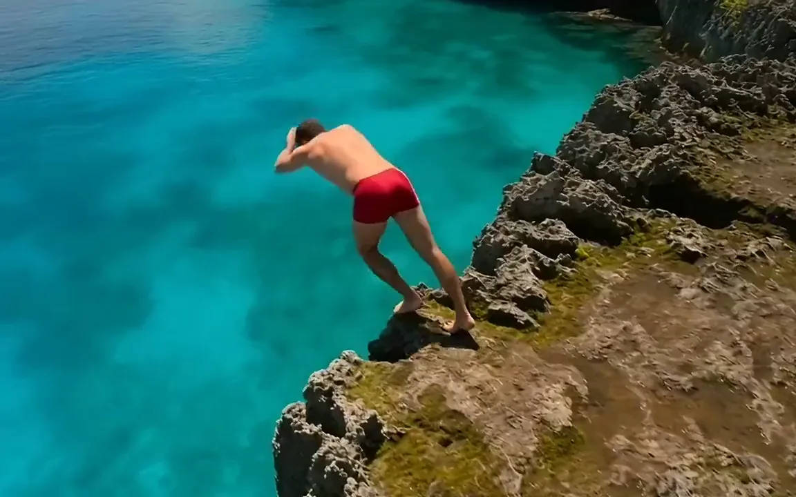 MiniMax H3 video of a cliff jumper in red shorts leaping from a rocky ledge into a turquoise lagoon