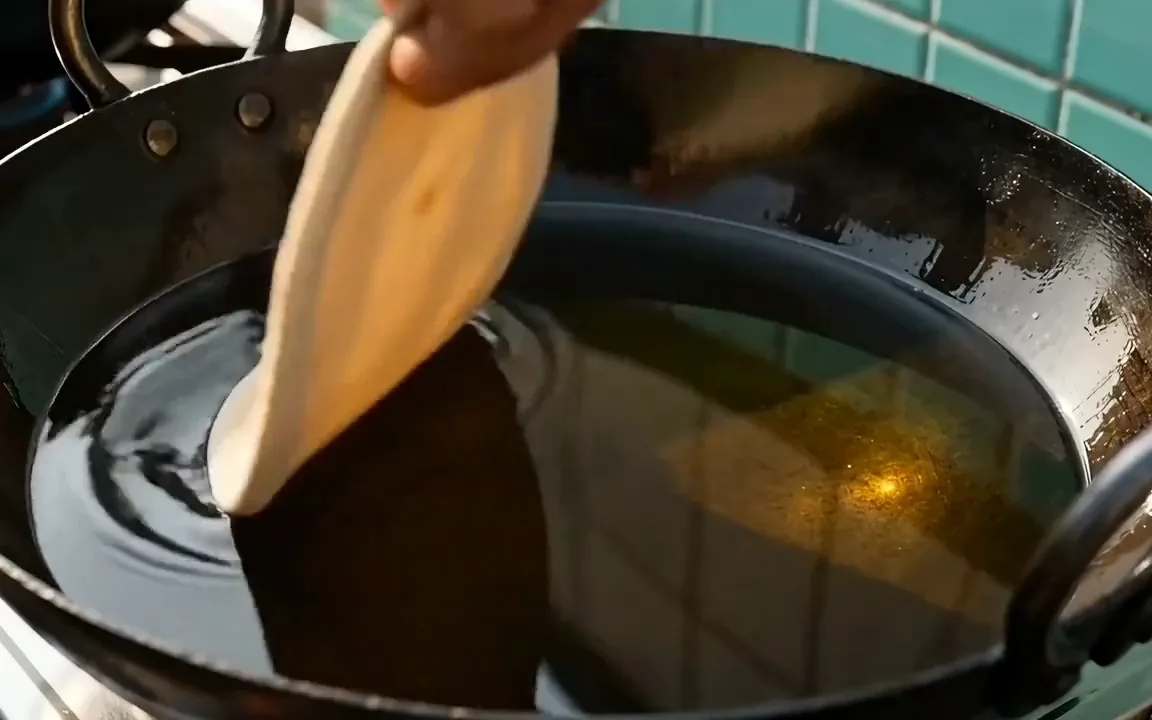 A disc of dough puffing up into a round golden puri in a black kadhai of hot oil
