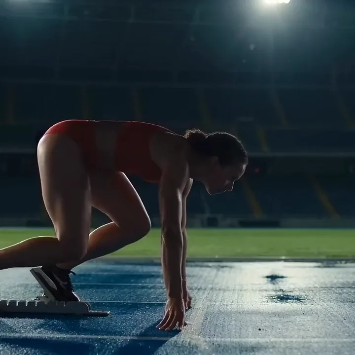 KI-Video einer Sprinterin in Rot, die auf einer nassen blauen Bahn aus dem Startblock schießt