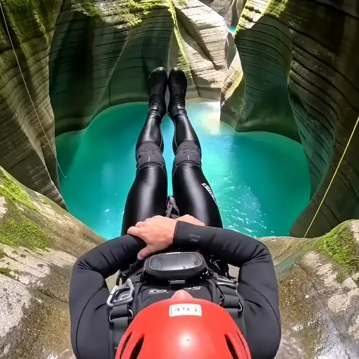 A canyoner in a red helmet sliding down a rock chute into a turquoise pool