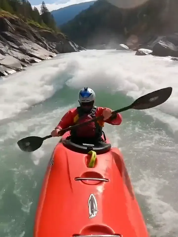 A kayaker in a red boat punching through white water on a mountain river