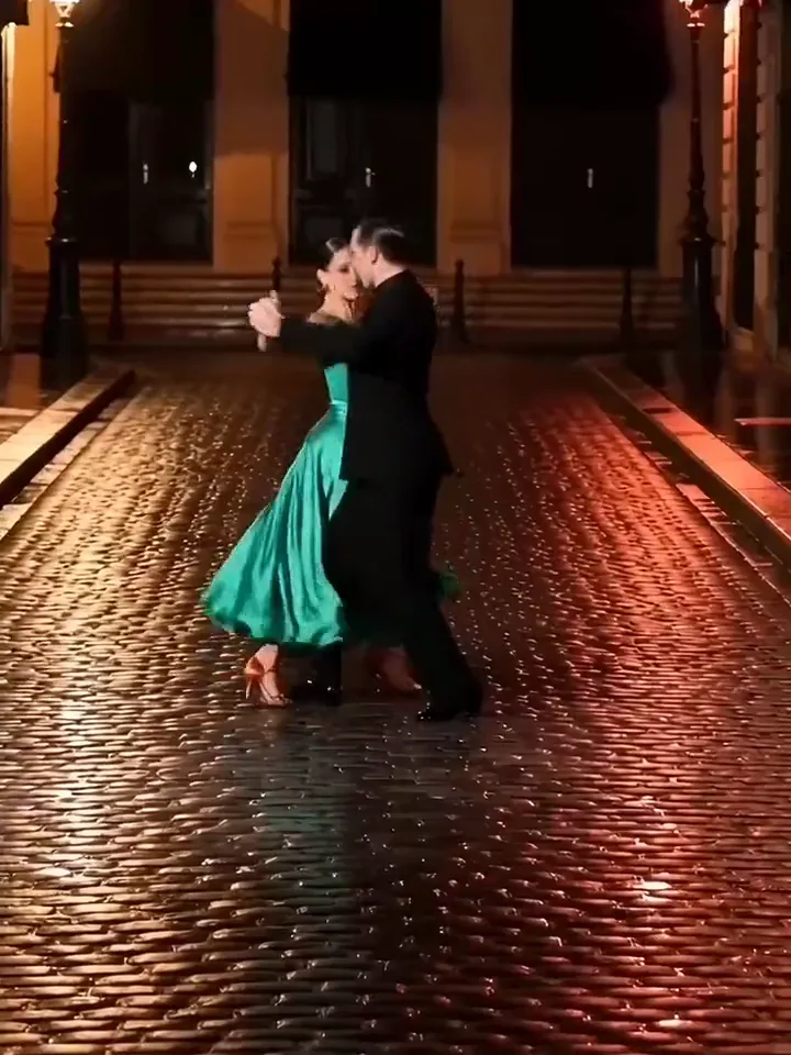 Tango couple in a green dress ending in a deep dip on a red lit cobbled street