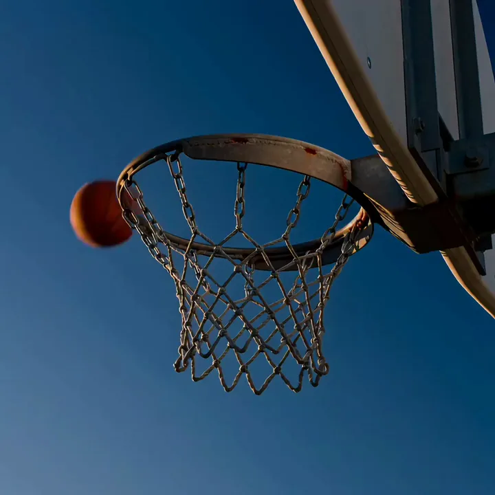 Un pallone da basket che cade attraverso una retina a catena contro un cielo blu intenso