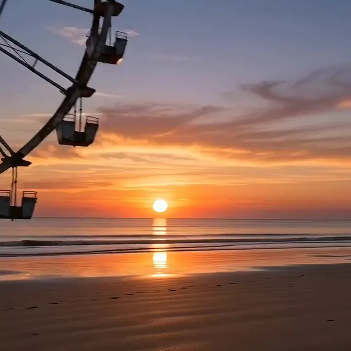 A Ferris wheel gliding along a beach at sunset with the sun glowing through its spokes