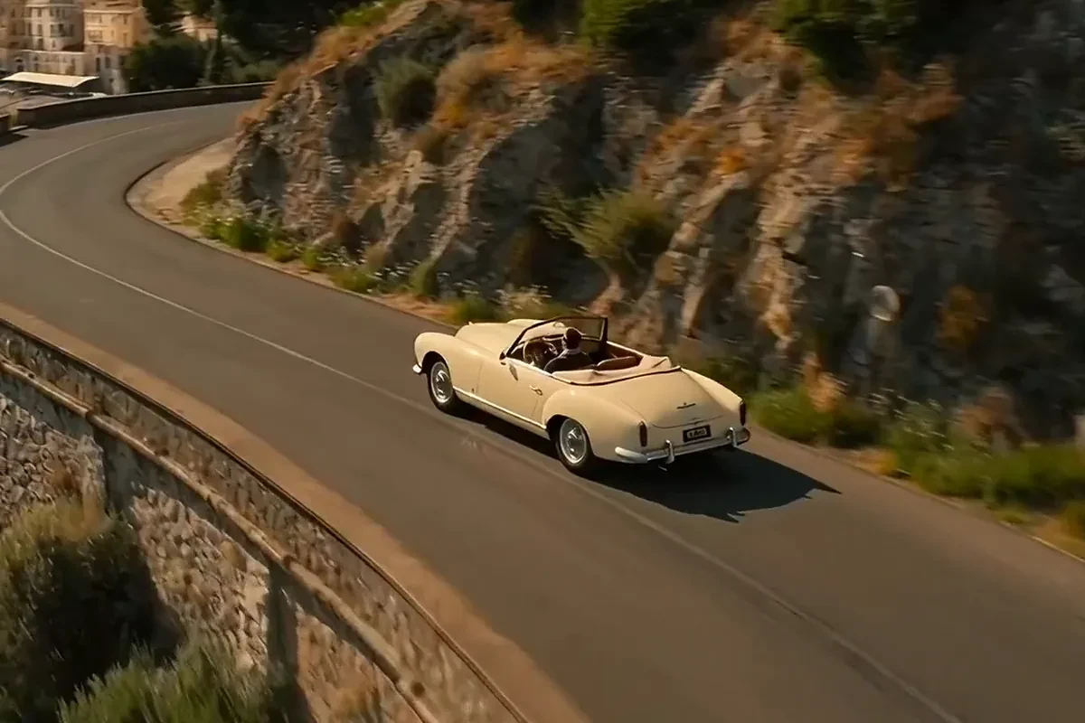 AI video generator clip of a cream 1960s cabriolet driving a cliff road above a turquoise Riviera harbour full of yachts