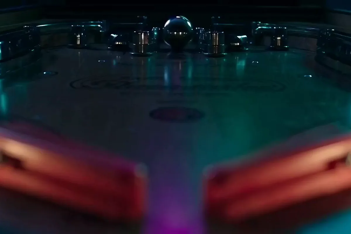 AI generated video of a silver pinball rolling toward a red flipper under pink lights