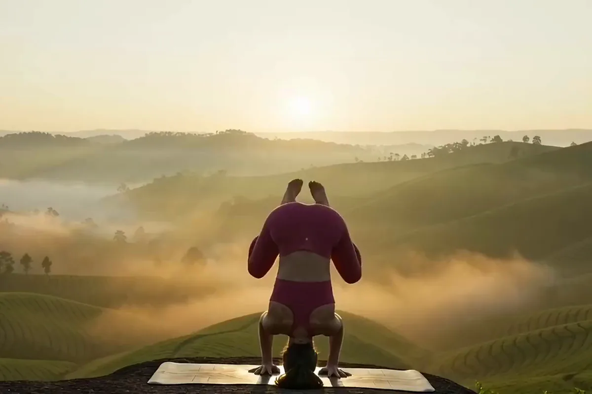 Gemini Omni video of a woman in magenta lifting into a straight yoga headstand on a mat above misty tea hills at sunrise