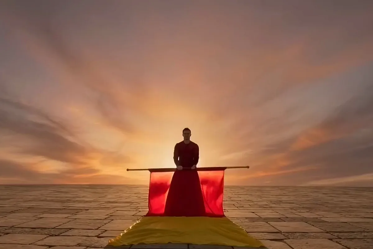A flag thrower in a red tunic tossing a red and yellow flag at sunset and catching it