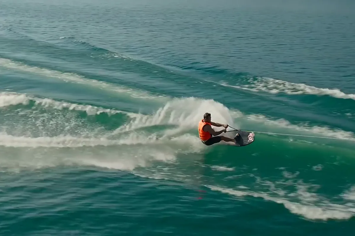 Kling AI video of a wakeboarder in orange throwing a tall arc of spray across a turquoise lake