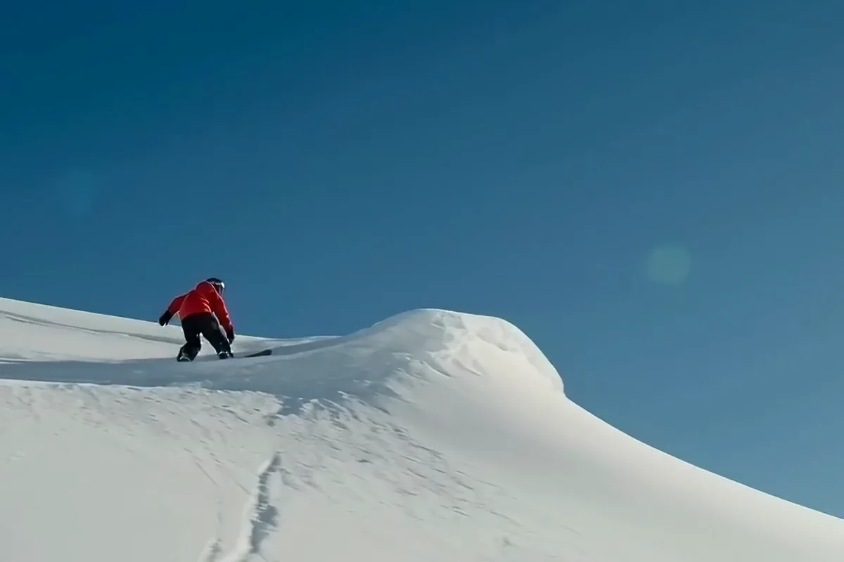 MiniMax H3 video of a snowboarder in a red jacket jumping off a snowy ridge and landing in a burst of powder