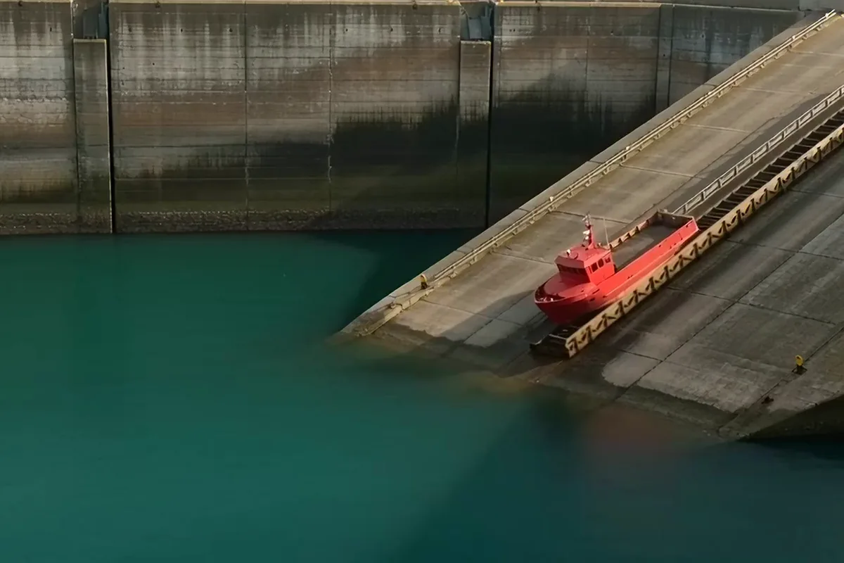 A small red ship sliding down a concrete slipway into a teal harbor with a splash