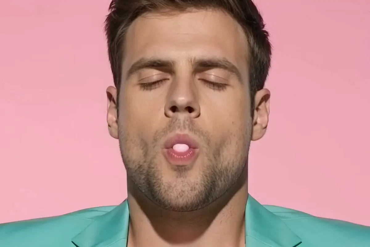 Man in a mint suit whose pink bubblegum bubble pops onto his nose against a pink wall