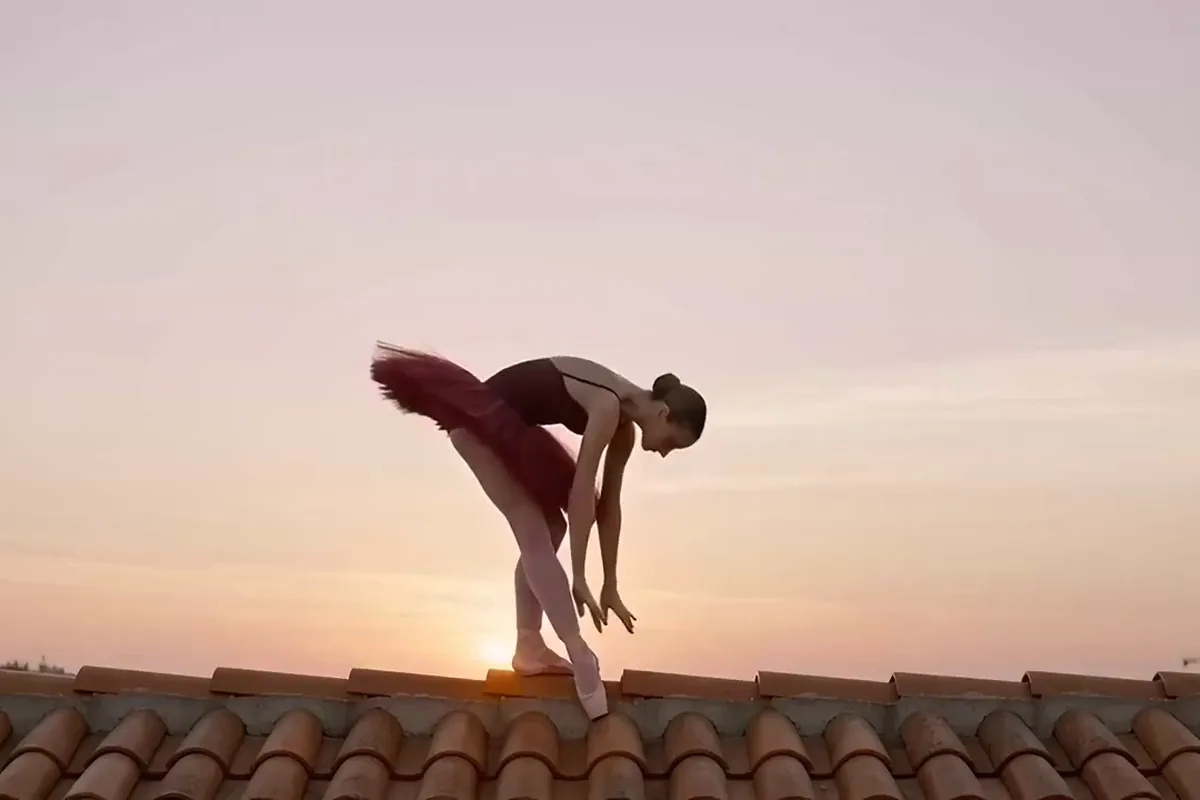 Seedance video of a ballerina in a crimson tutu rising from a bow into an arabesque on a rooftop at sunrise