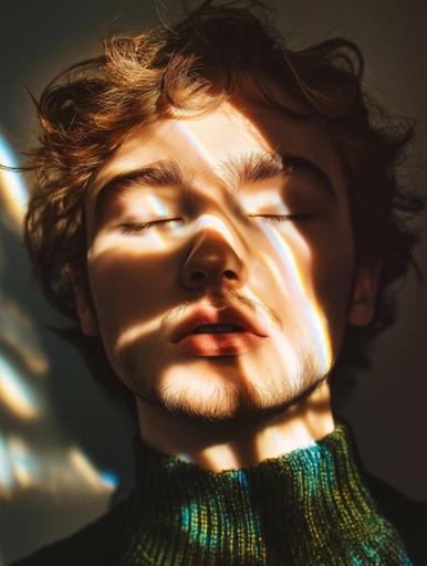 A young man with light olive skin and short, wavy brown hair closes his eyes as gentle sunlight creates soft rainbow patterns across his face and the background, while he wears a dark green sweater that contrasts with the muted backdrop. The sunlight casts warmth on his complexion, and the image captures a dreamlike mood through the interplay of natural light and prism-like reflections, highlighting his serenity.