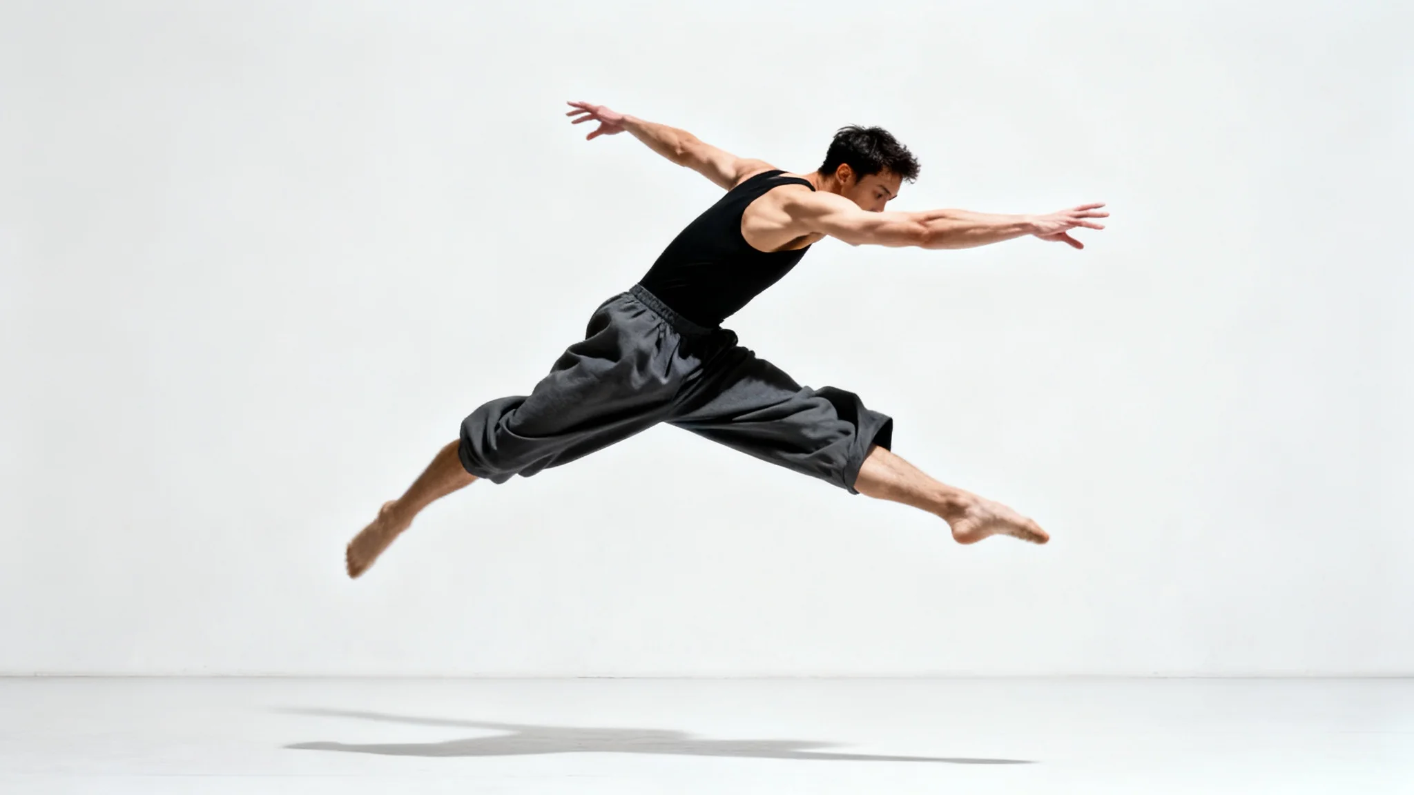 A contemporary dancer frozen in a dynamic mid-air leap against a stark white background, showcasing athleticism and grace.