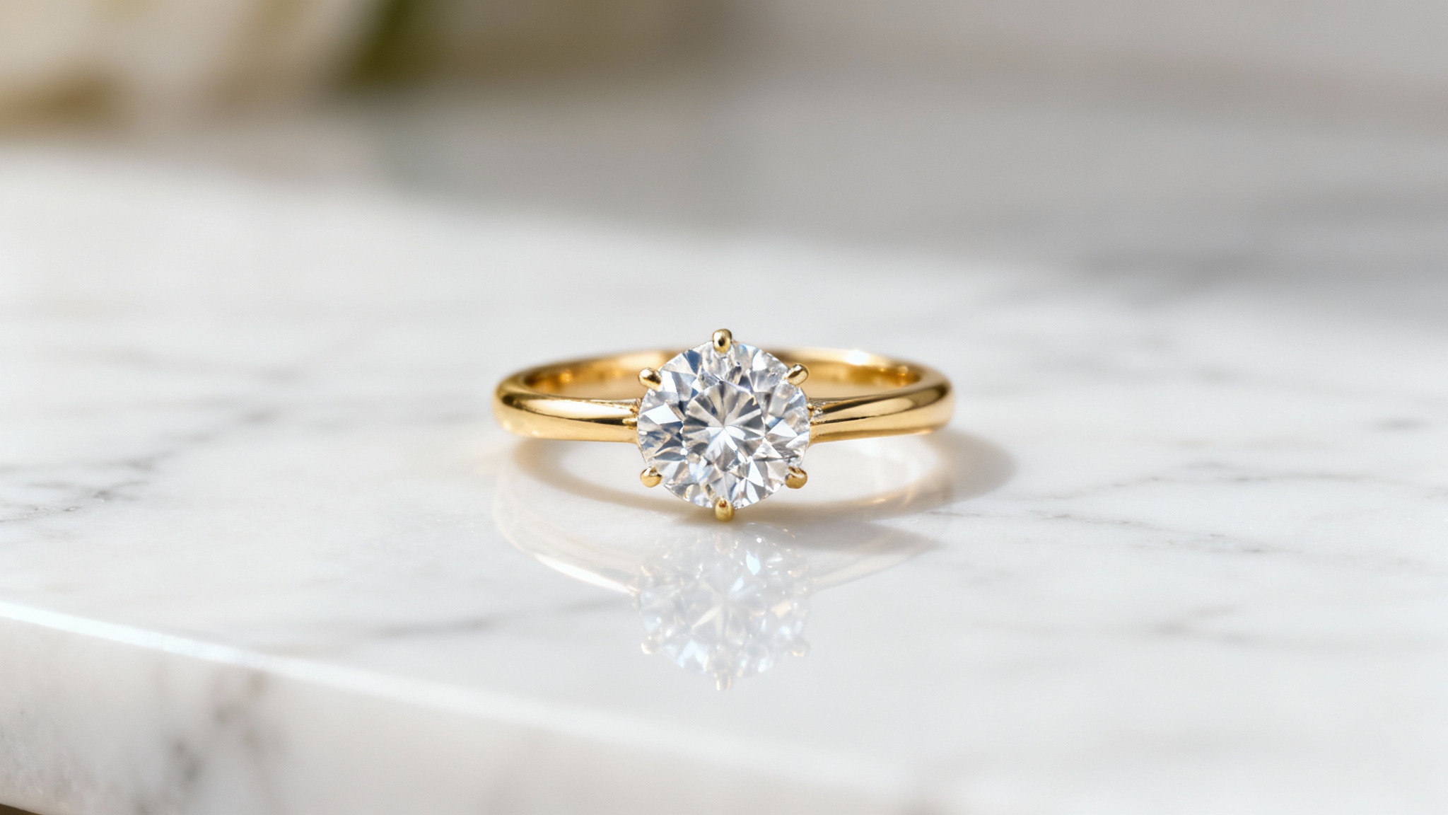A professional, close-up studio photograph of a gold and diamond engagement ring resting on a white marble surface, showcasing a polished e-commerce look.