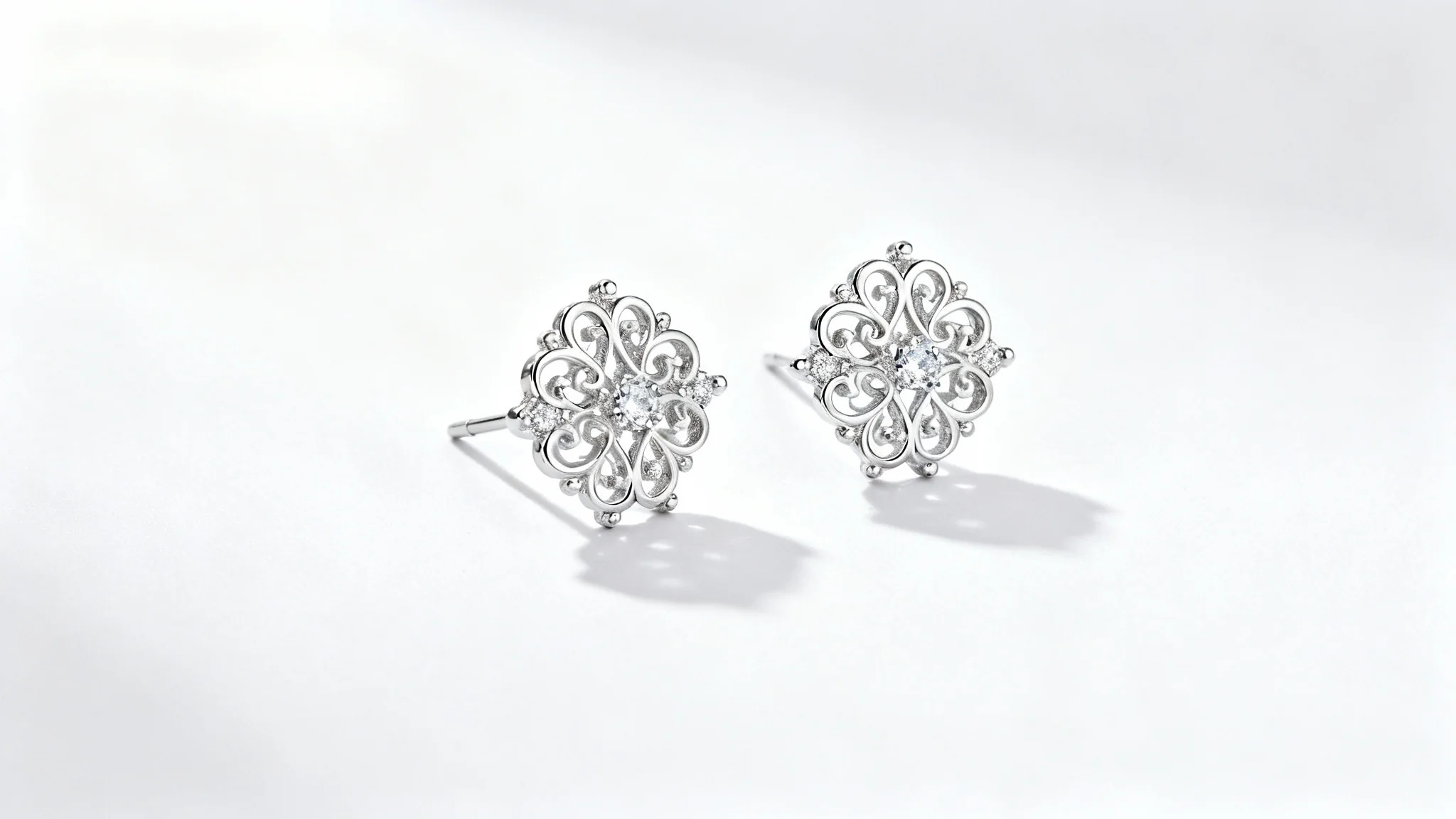A professional jewelry photograph of elegant silver filigree earrings with small diamonds, shot in a studio with soft lighting on a clean white background.