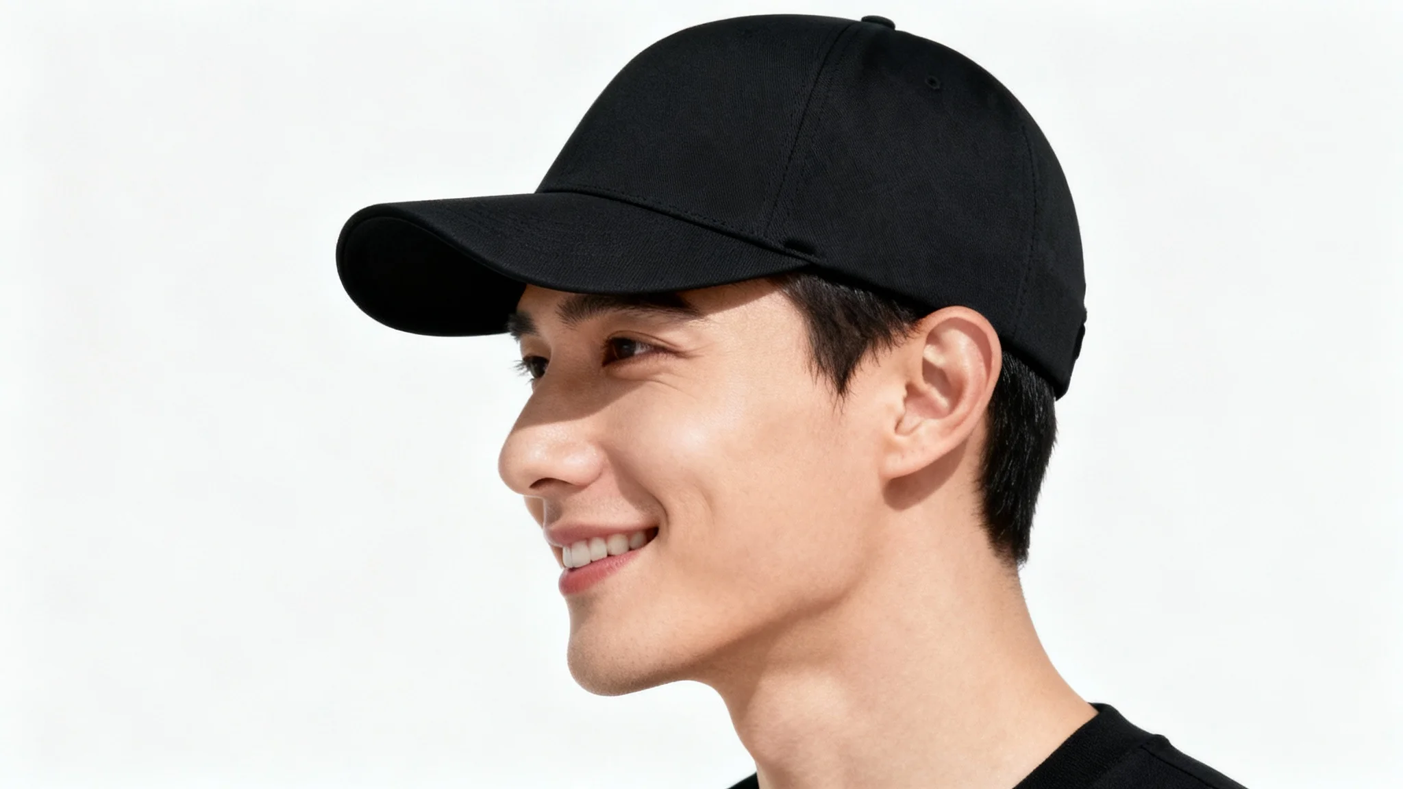A close-up, side-profile photo of a person smiling while wearing a modern black baseball cap against a plain white background.