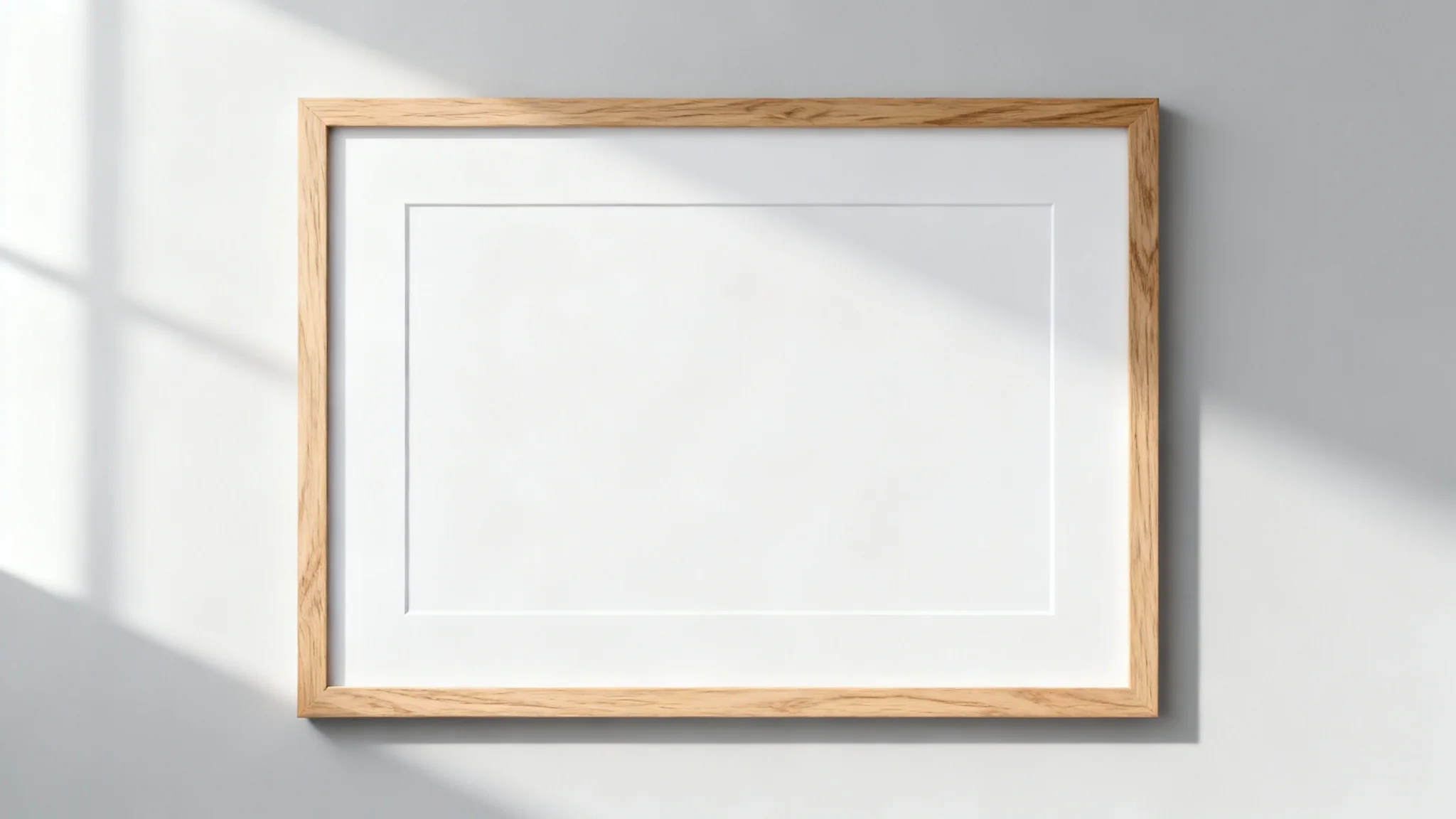 A minimalist, light oak landscape frame mockup with a white mat, hanging on a plain light gray wall in a brightly lit room.