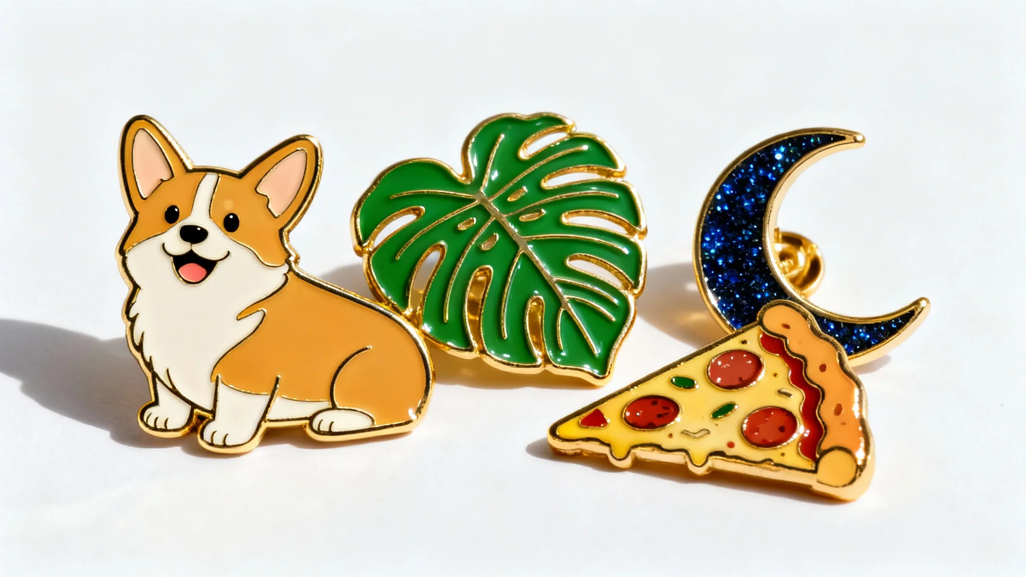 A photorealistic mockup of four custom-designed hard enamel pins with gold plating, displayed on a clean white background. The pins feature designs of a cute corgi, a monstera leaf, a glittery crescent moon, and a slice of pizza.