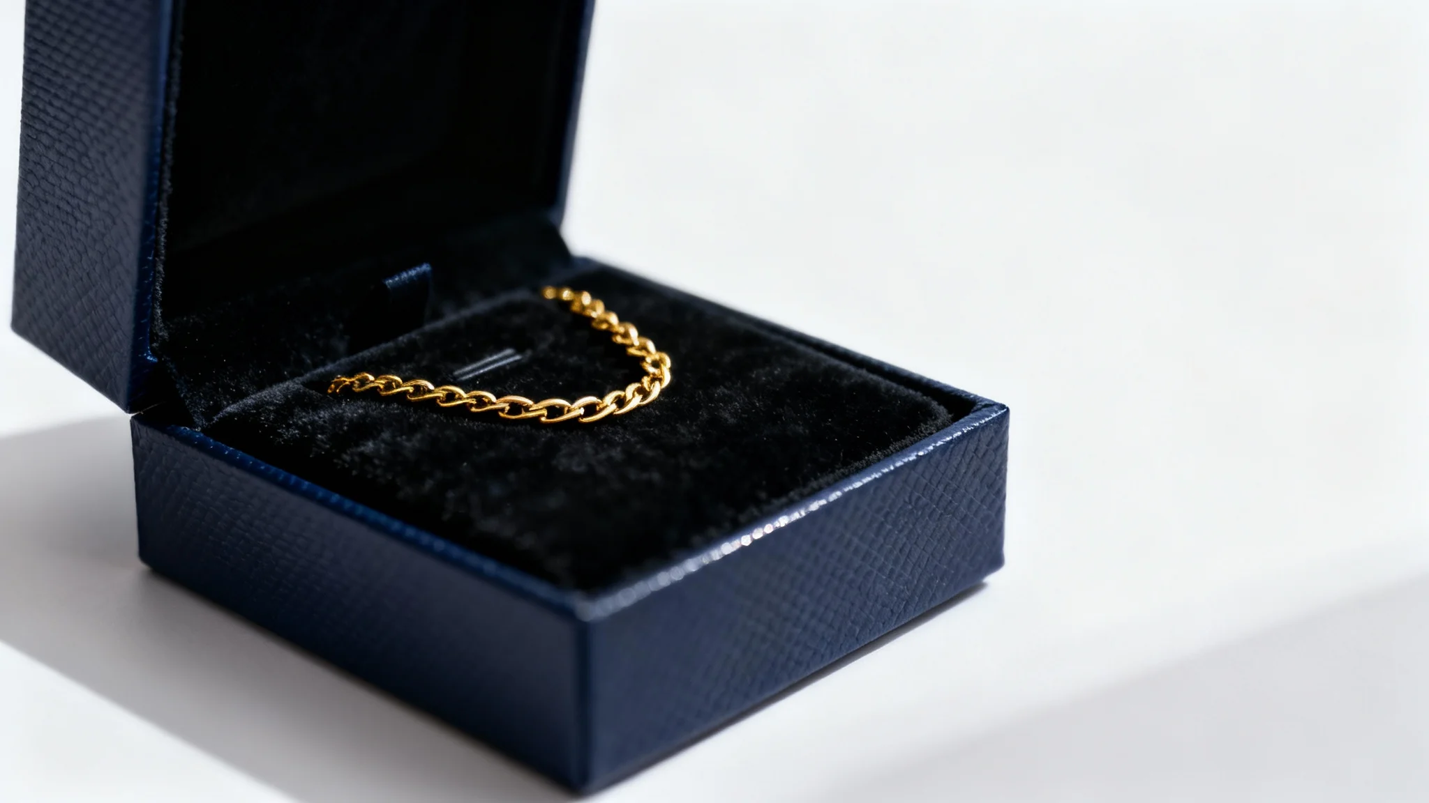 An elegant, dark navy blue jewelry gift box, slightly open to reveal a delicate gold necklace resting on a black velvet interior, shot against a plain white background.