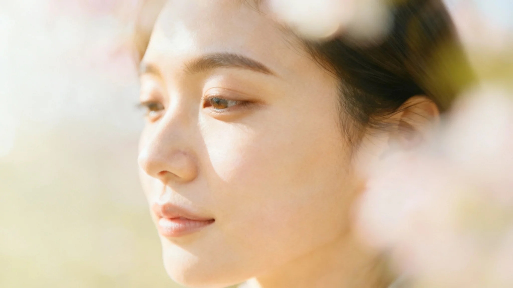 A close-up portrait of a woman with a serene expression, rendered in a soft focus style that gives the image a dreamy, ethereal quality. The lighting is warm and gentle, and the background is a soft blur of pastel colors.