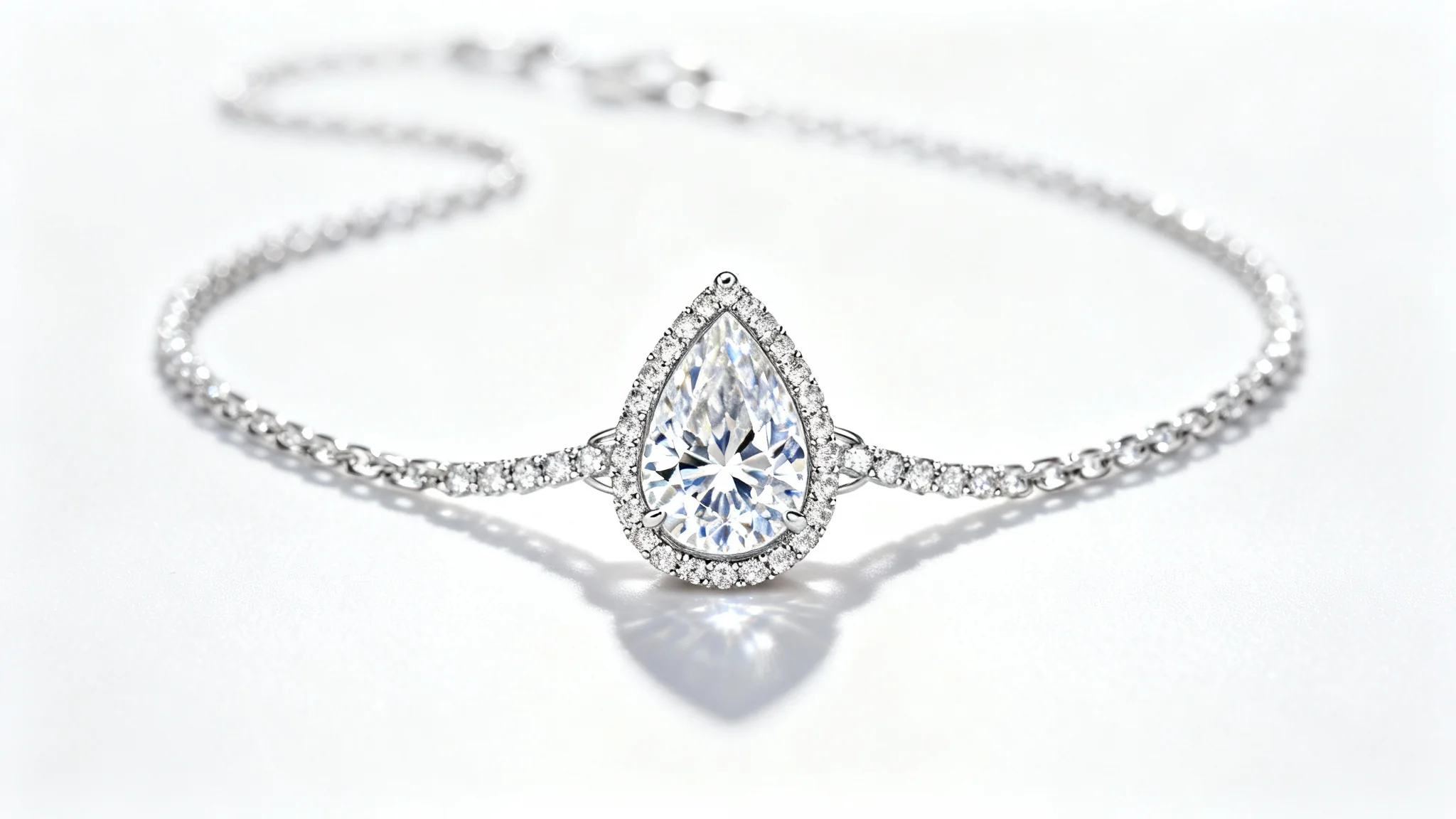 A studio photograph of an elegant platinum diamond necklace with a pear-shaped central stone, lying on a clean white background.