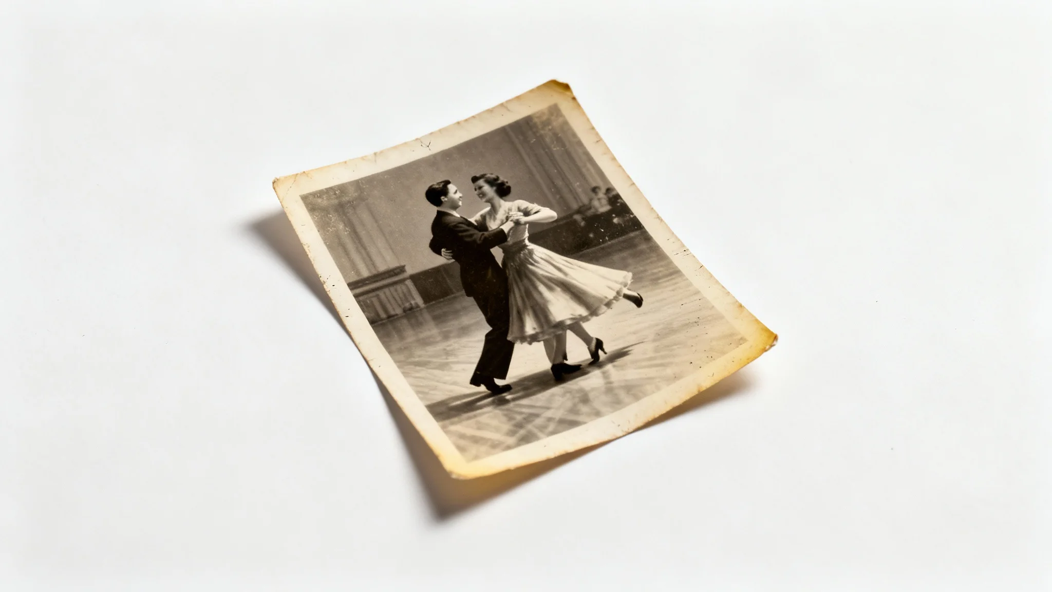 A vintage sepia photograph of a couple dancing, showing signs of age like faded color and worn edges, displayed on a clean white background.