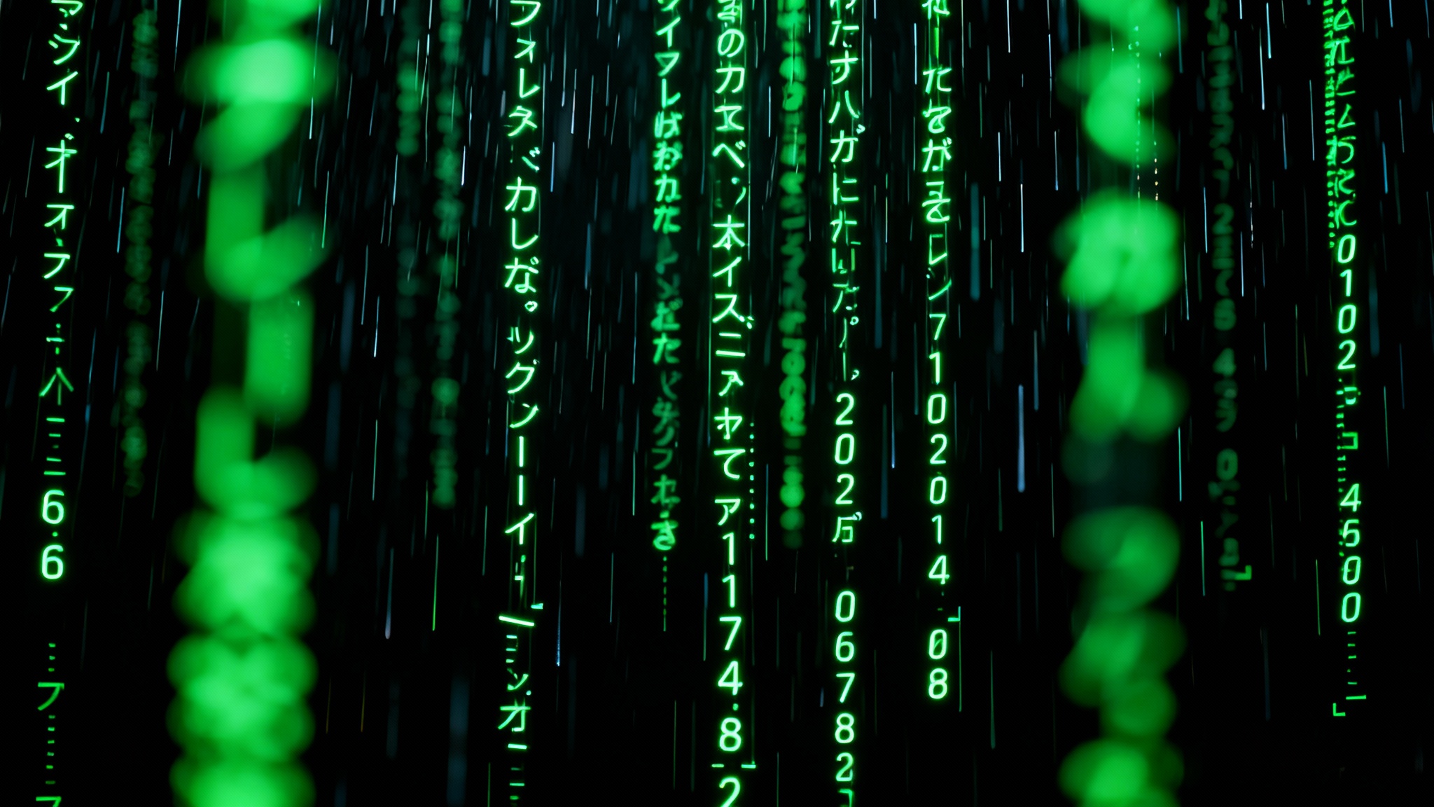 A high-resolution image displaying a green digital code rain effect, reminiscent of the Matrix, with cascading streams of glowing green characters on a black background.