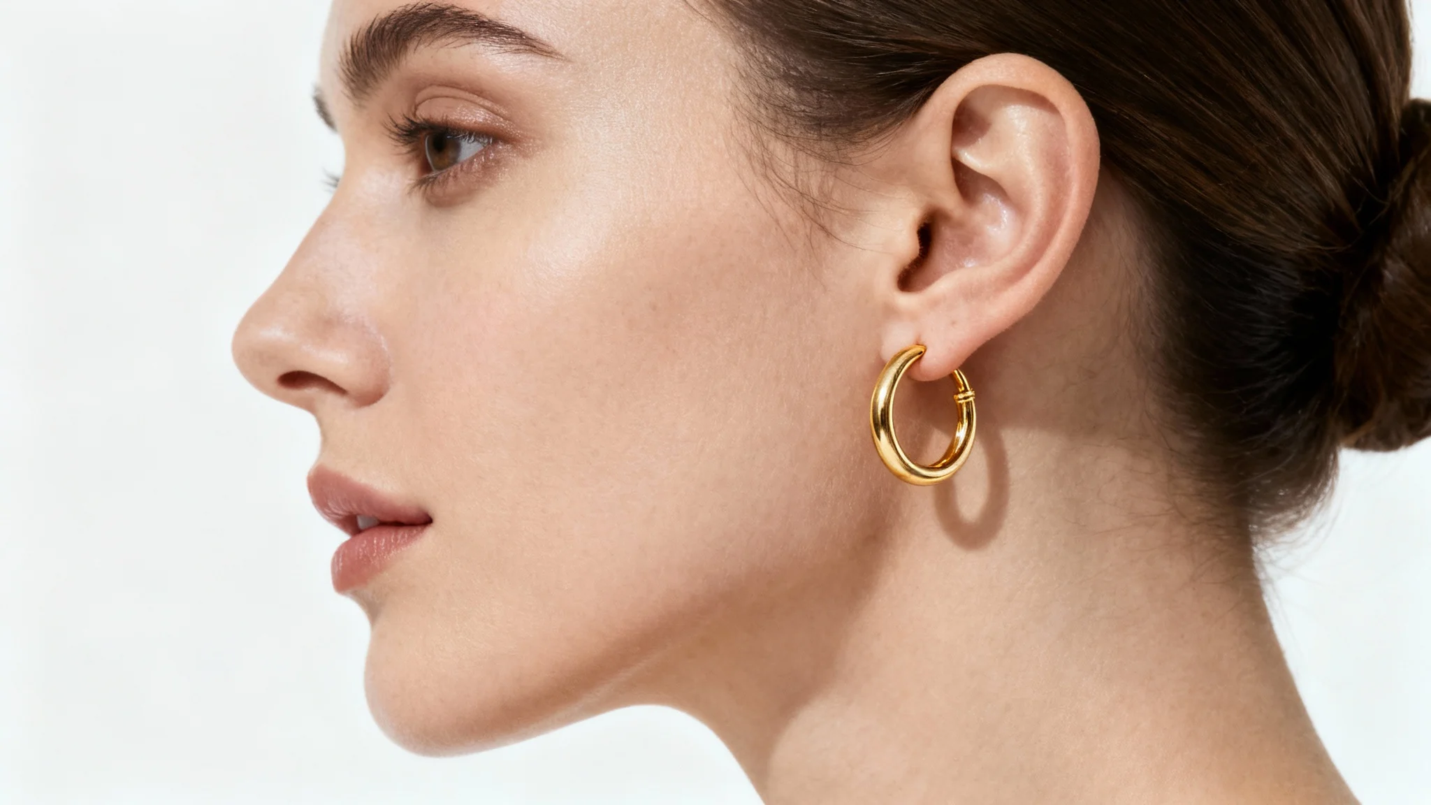 A hyper-realistic close-up image of a woman's ear, demonstrating a virtual earring try-on with a beautiful gold hoop, set against a stark white background.