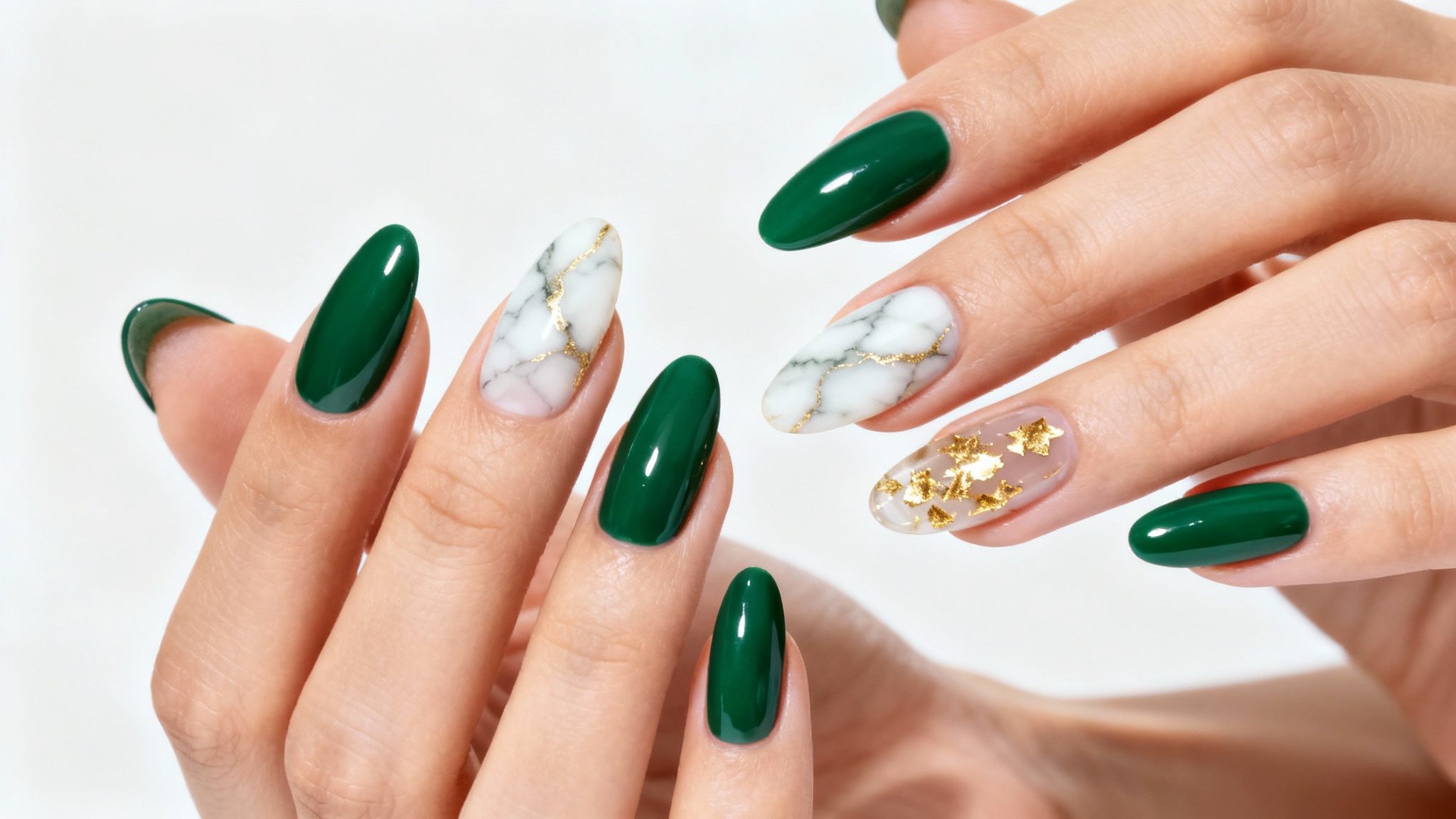 A close-up photo of a woman's hands with expertly manicured almond-shaped nails, featuring an elegant design in emerald green, white marble with gold veins, and gold leaf accents, set against a clean white background.