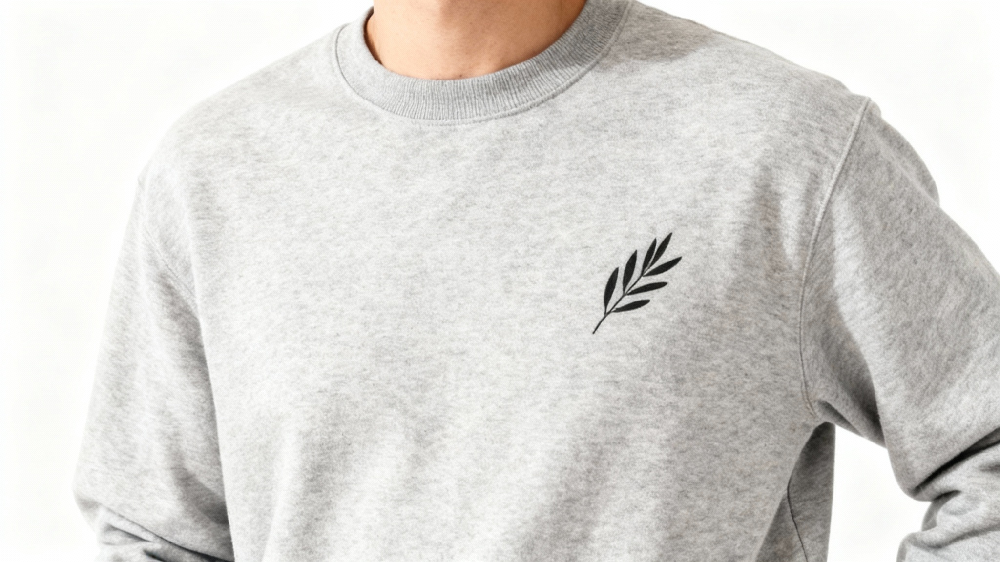 A close-up of a person wearing a heather gray minimalist sweatshirt, showcasing a small, elegant black line drawing of an olive branch on the chest.