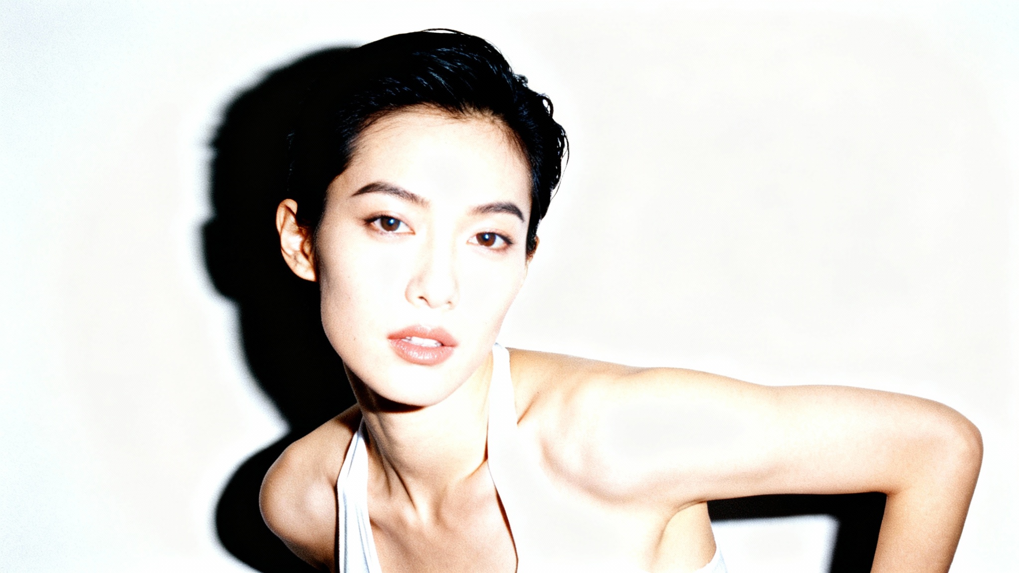 A stylish person photographed with a direct, harsh camera flash, creating bright highlights and a distinct shadow behind them against a white background.