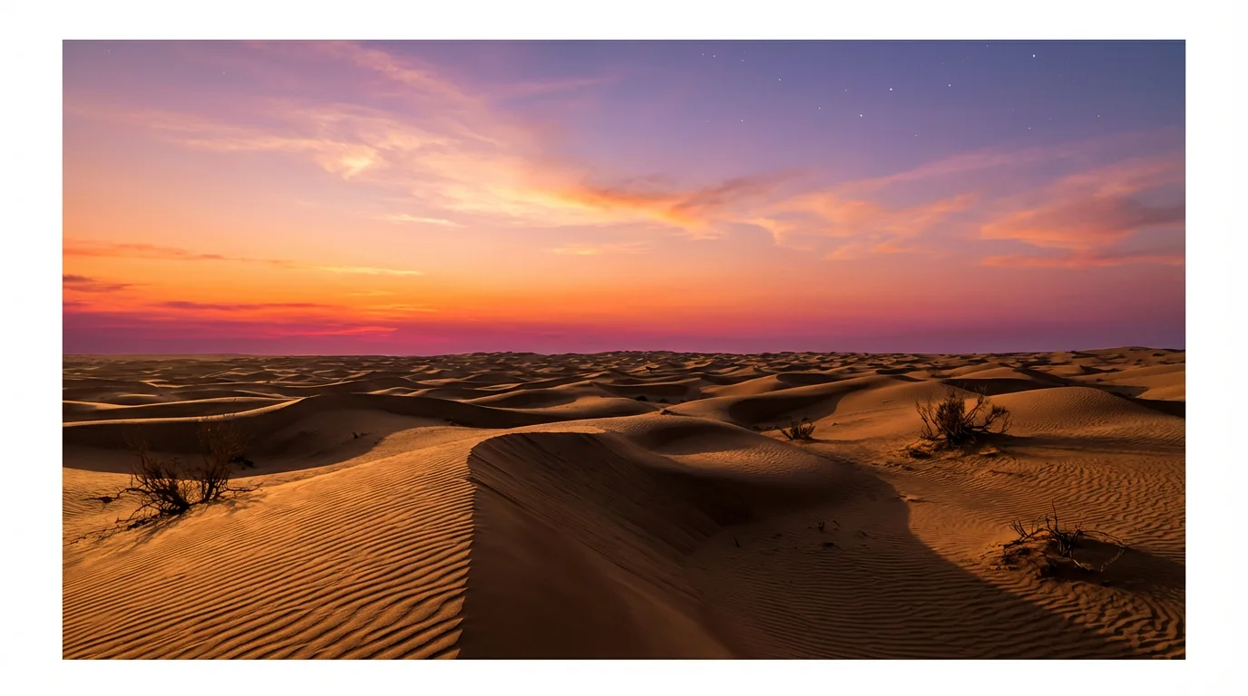 A photorealistic image of a vast desert at sunset. The sky is a brilliant mix of orange, pink, and purple, with stars beginning to appear. Rolling sand dunes stretch to the horizon, catching the warm, golden light.