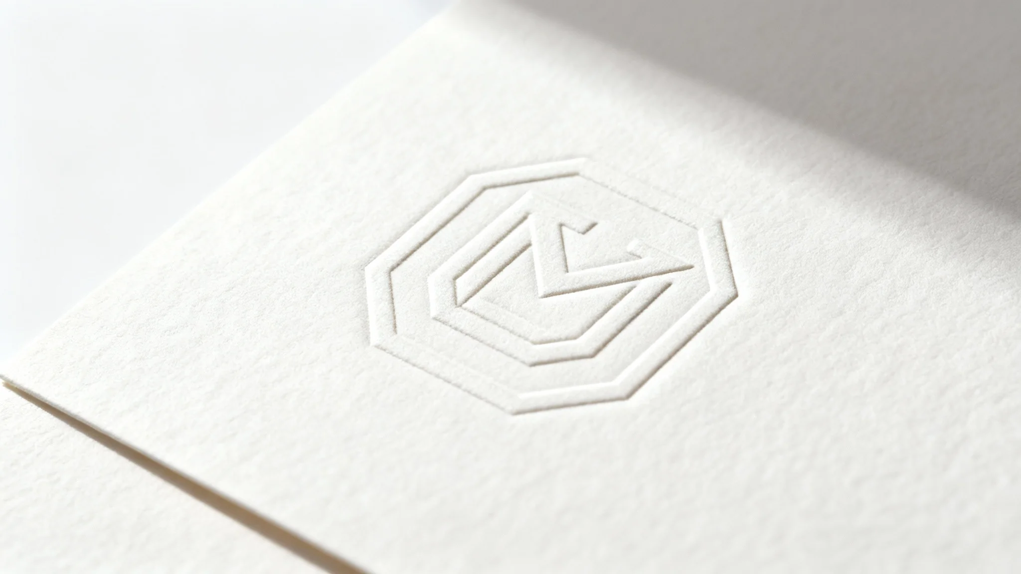 A close-up, professional photograph showing an elegant logo debossed into thick, textured off-white paper against a clean white background, highlighting the tactile quality of the effect.