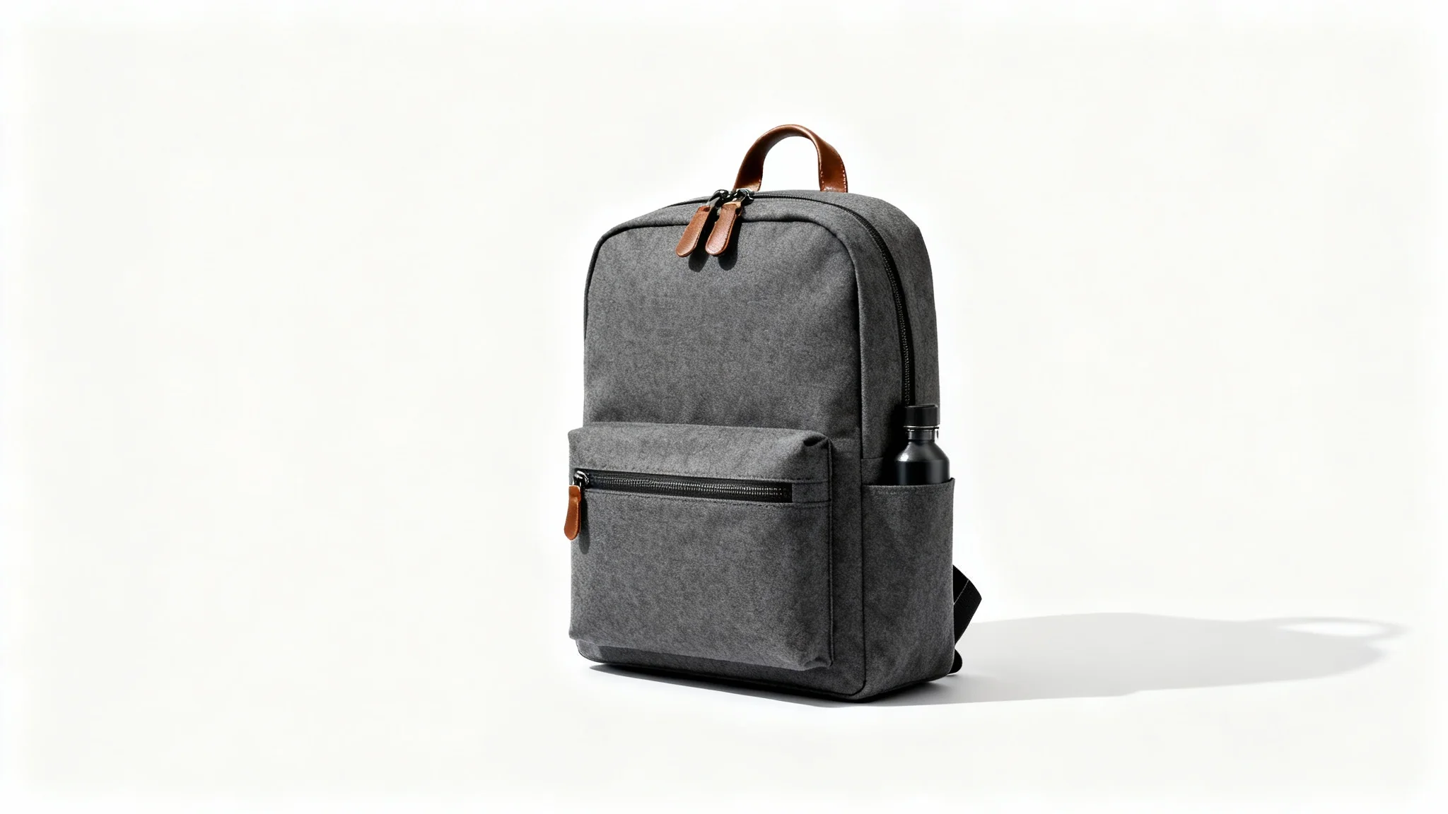 A modern, minimalist backpack in charcoal gray canvas with brown leather details, standing on a clean white background in a professional product shot.