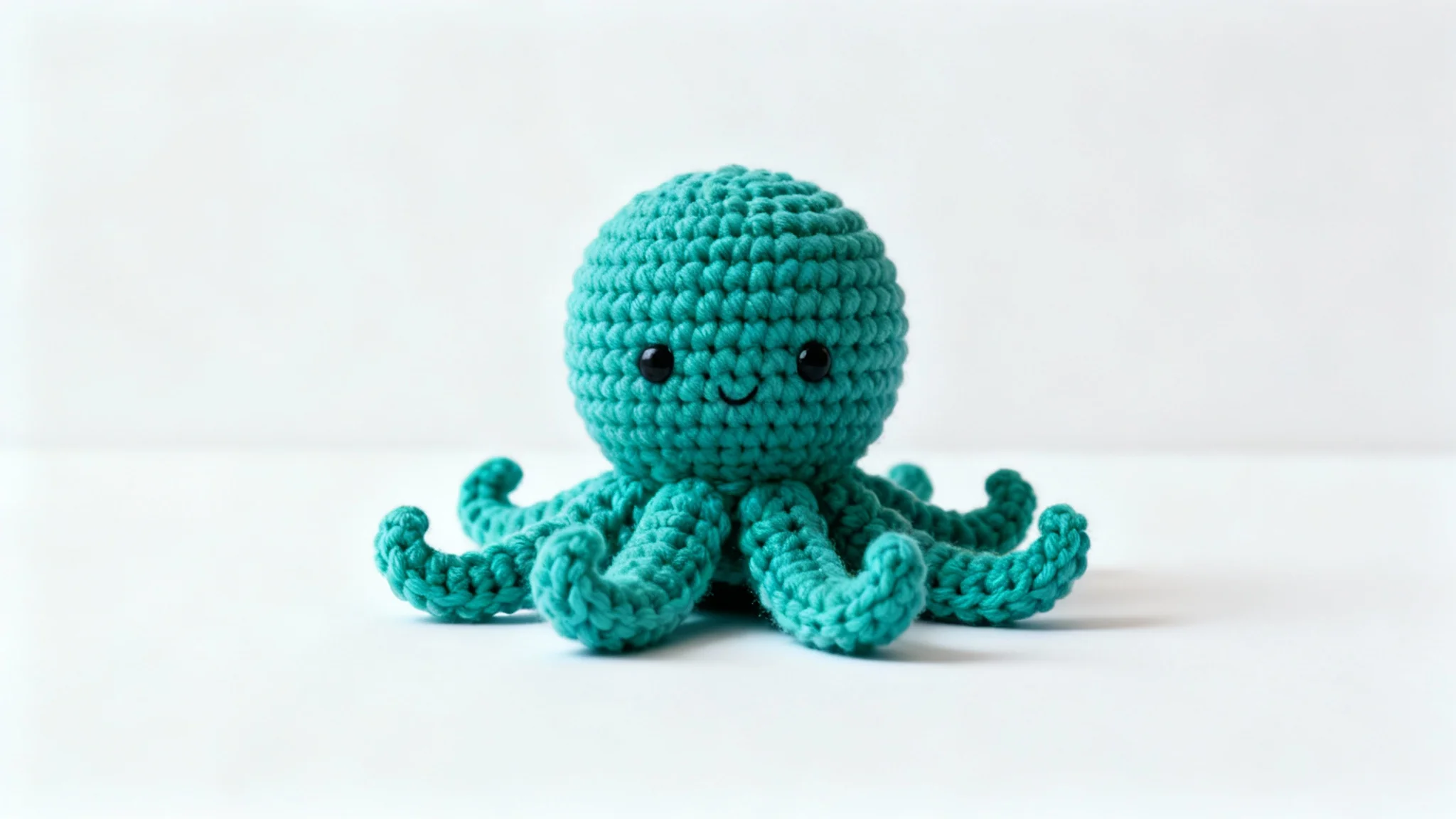 A beautifully crocheted octopus toy in a vibrant teal color, sitting on a white background, showcasing the final result of a crochet pattern.