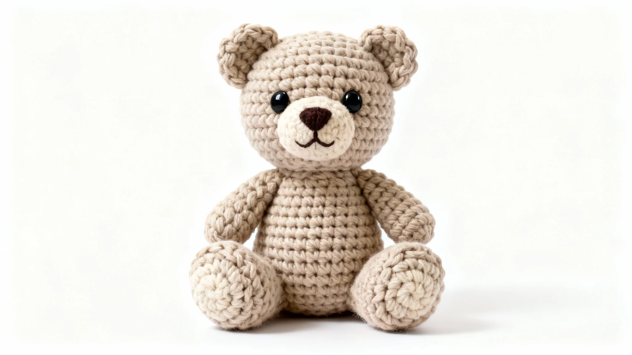 A close-up photograph of a cute, hand-crocheted teddy bear made from oatmeal-colored yarn, sitting against a clean white background, representing a finished crochet pattern.