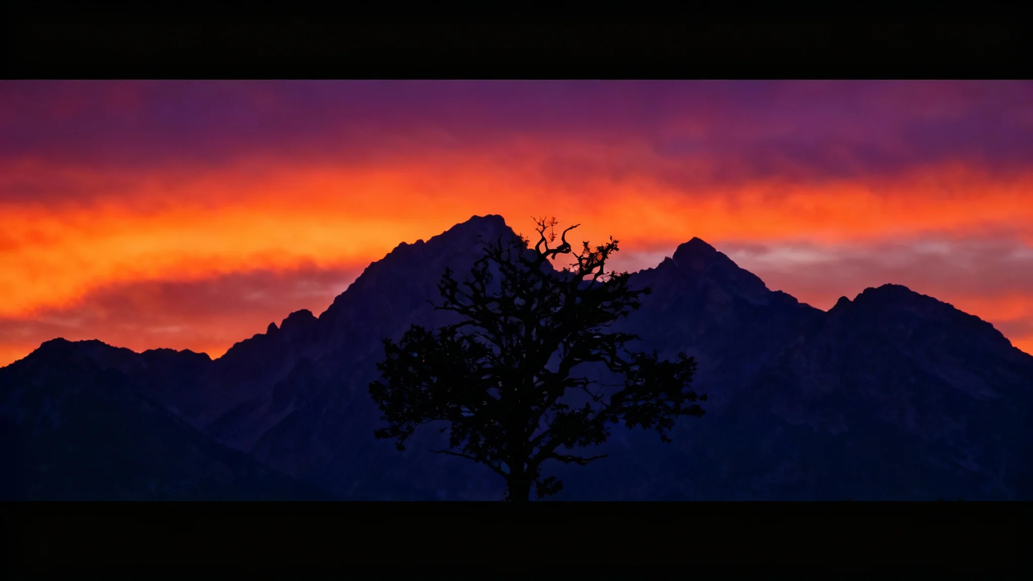 A dramatic mountain landscape at dusk, displayed in a cinematic widescreen format with black bars on the top and bottom, creating a film-like effect.