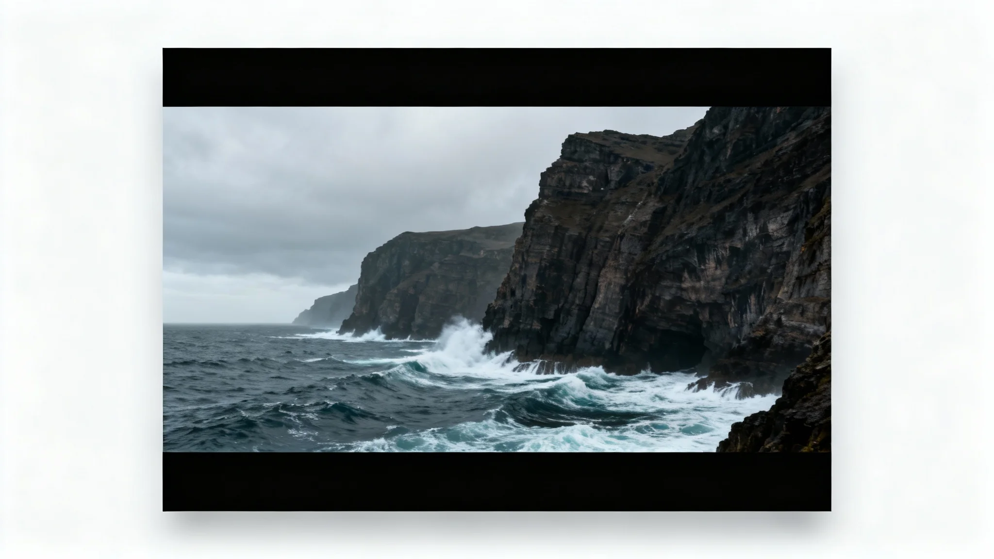 A photorealistic photograph of a dramatic coastline, presented with cinematic black bars at the top and bottom to create a widescreen effect, set against a plain white background.