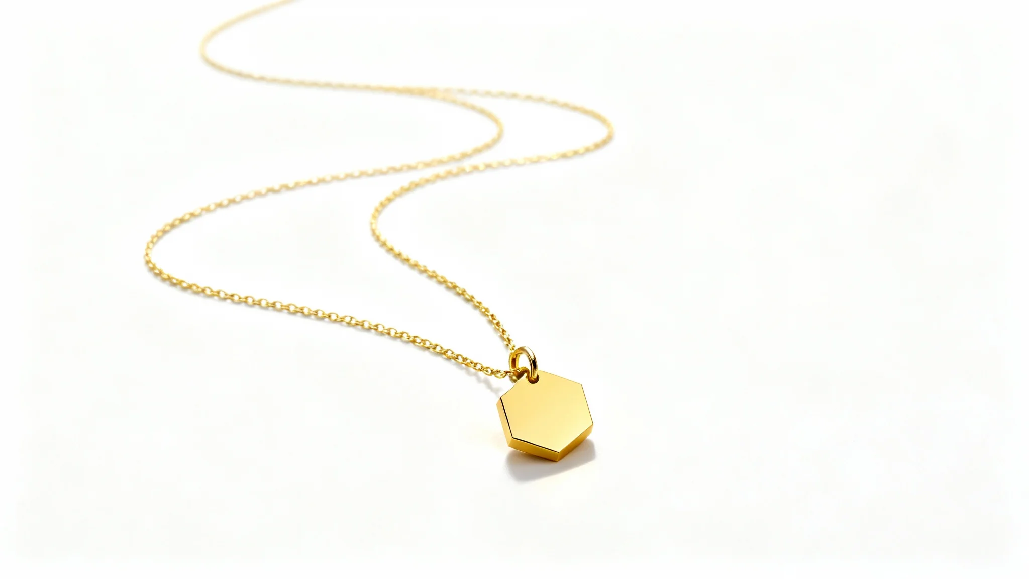 A professional product mockup of a delicate gold necklace with a small hexagonal pendant, elegantly curved on a clean white background.