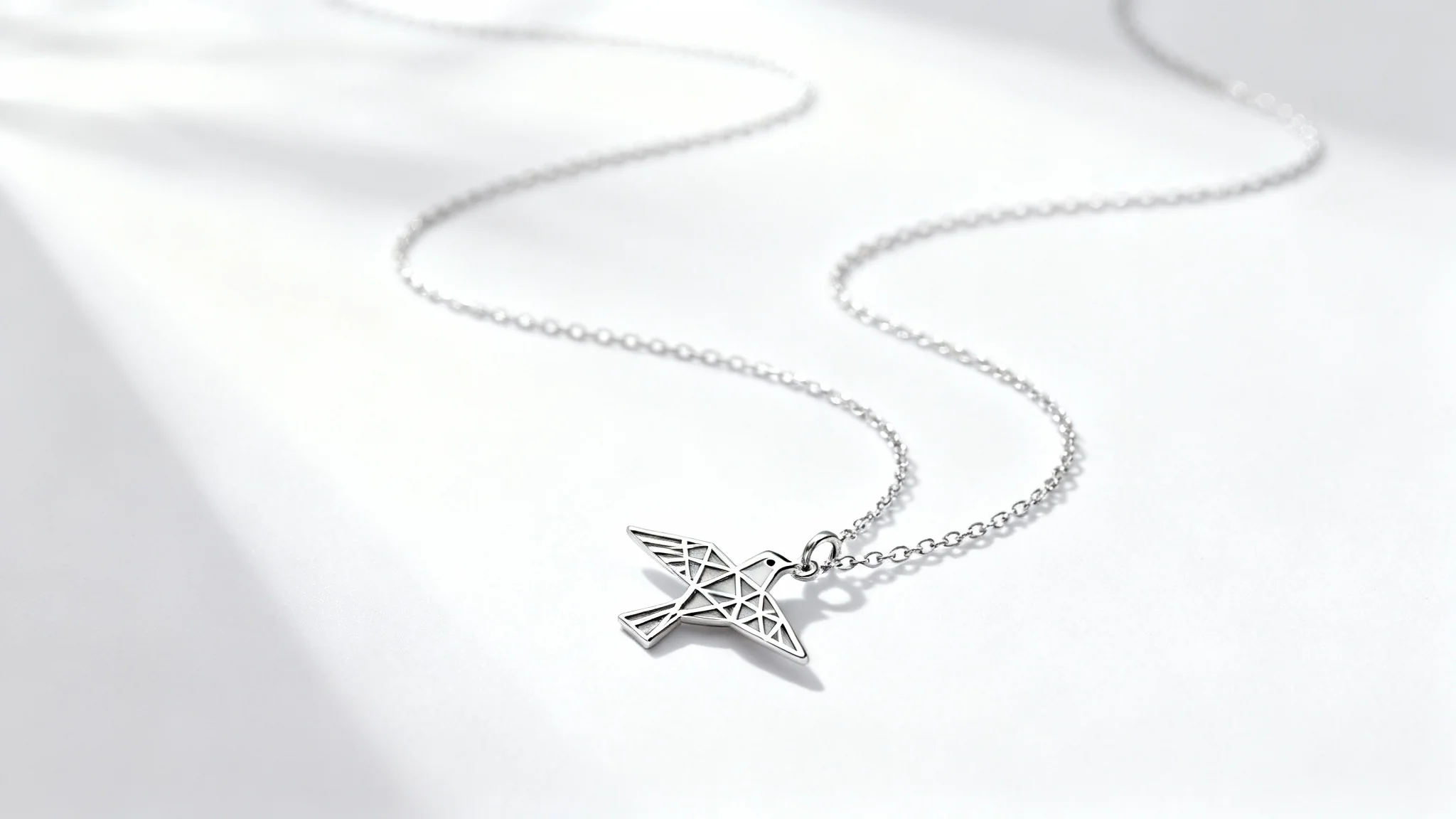 A photorealistic mockup of a delicate silver necklace with a geometric bird pendant, elegantly displayed on a clean white background.