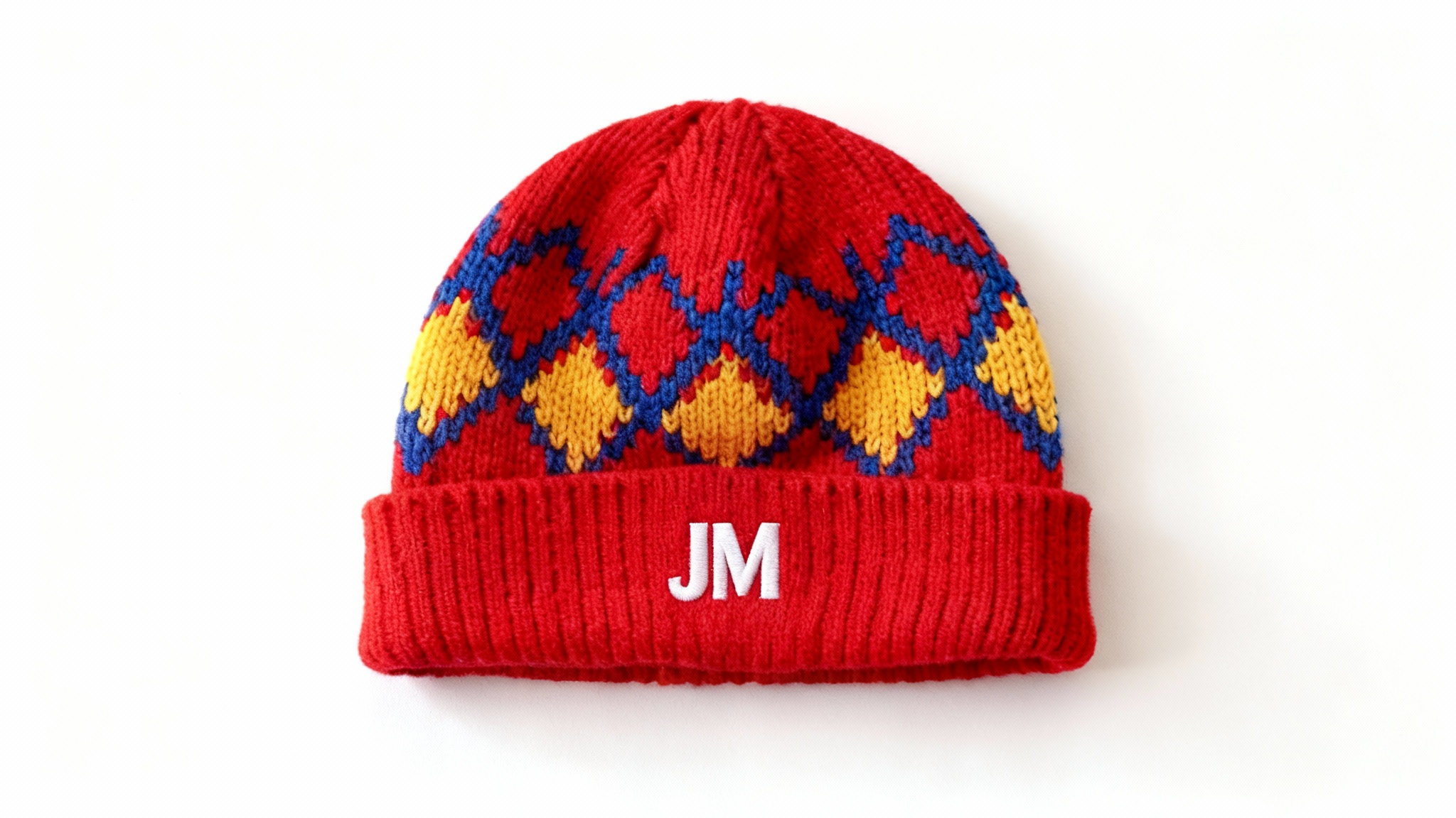 A professionally photographed vibrant red beanie with a blue and yellow geometric pattern, featuring a custom white embroidered logo of the initials 'JM' on the cuff, displayed on a white background.