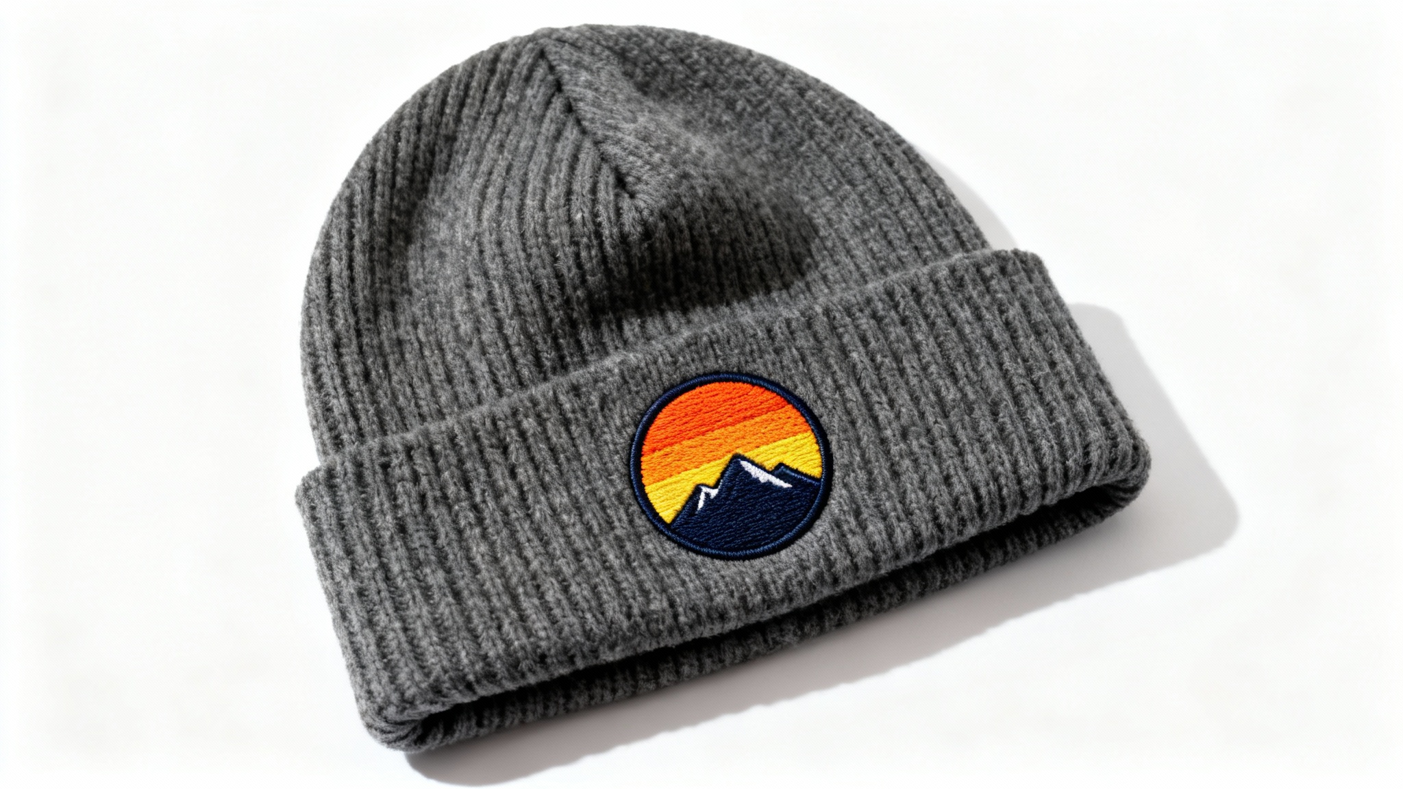 A close-up product shot of a charcoal grey knit beanie with a custom embroidered patch of a mountain sunset on its cuff, displayed against a clean white background.