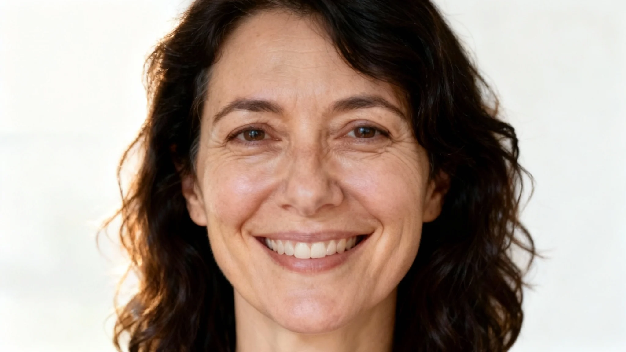 A close-up portrait of a smiling woman with smooth, refreshed skin under her eyes, showcasing the effective result of an eye bag removal tool.