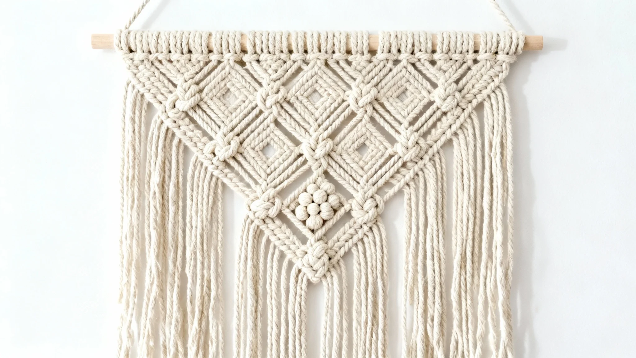 A detailed photograph of a complex macrame wall hanging with intricate geometric patterns and long tassels, displayed against a solid white background.