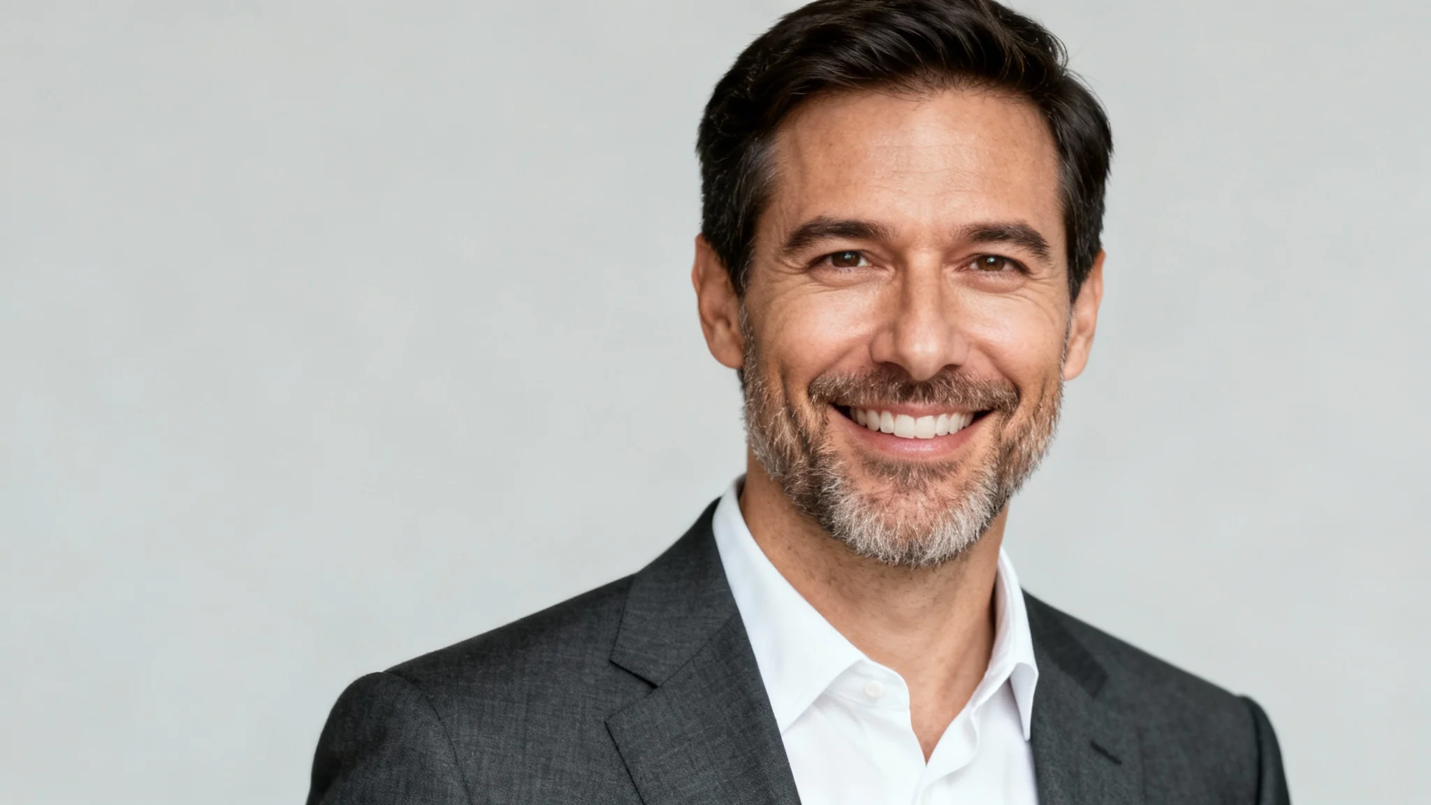 A hyper-realistic professional headshot of a smiling man in a suit against a plain light grey background, representing an AI-generated corporate portrait.