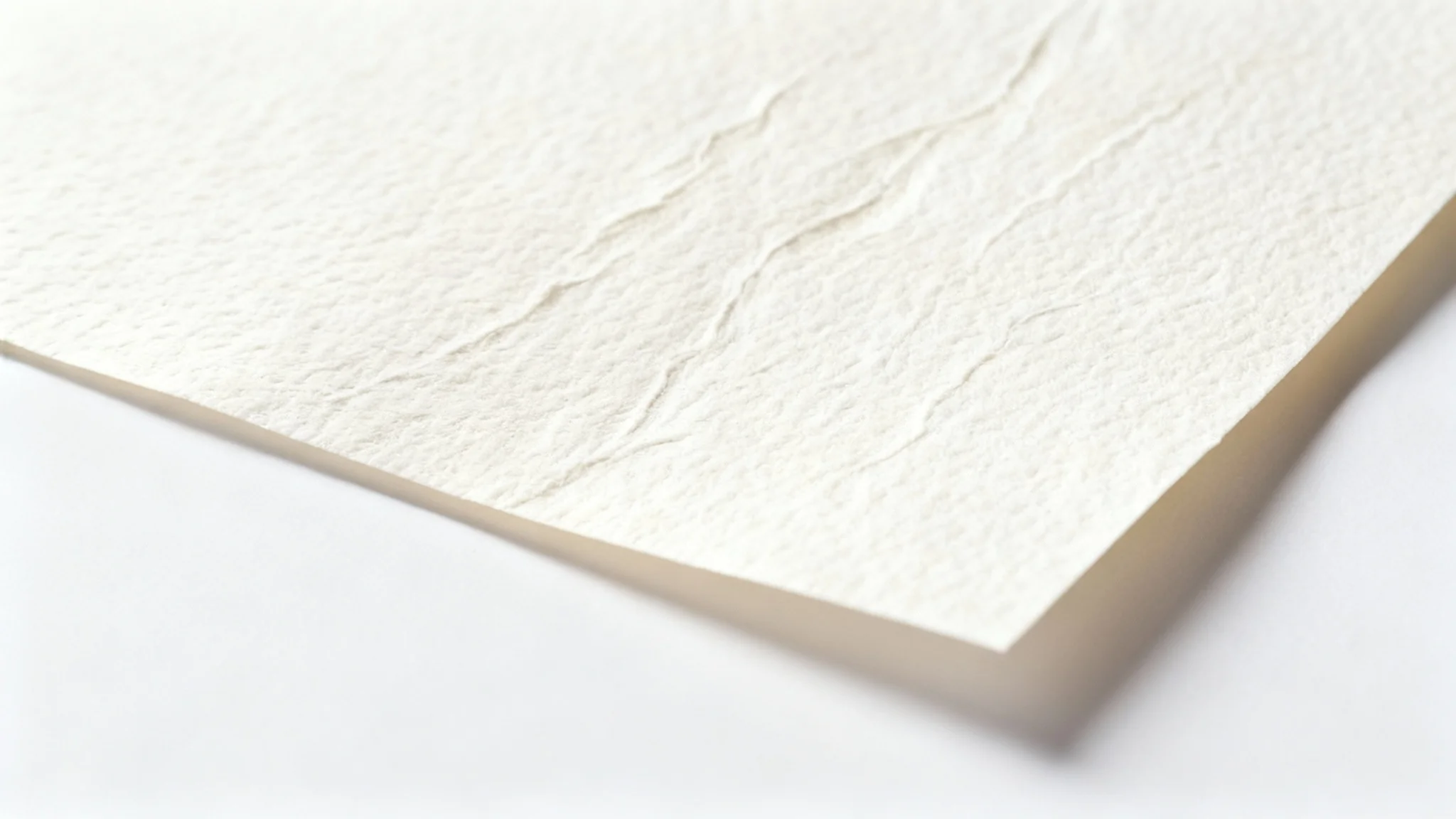 A detailed macro photograph of a sheet of textured, off-white watercolor paper on a clean white background, highlighting its rough grain and fibrous quality.