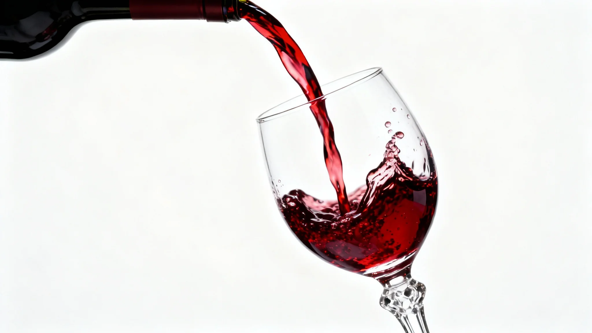 A dynamic and elegant close-up photograph of red wine being poured into a crystal glass, with the splash frozen in motion, set against a stark white background.